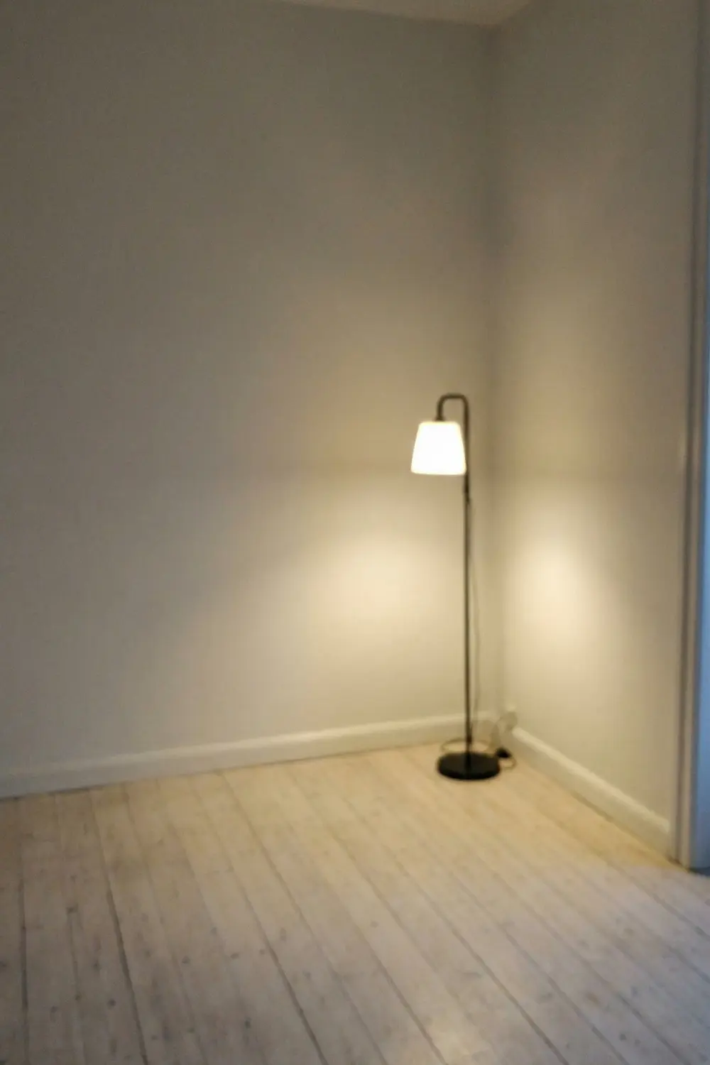 Minimal empty corner decor with tall black floor lamp warm glow and white walls
