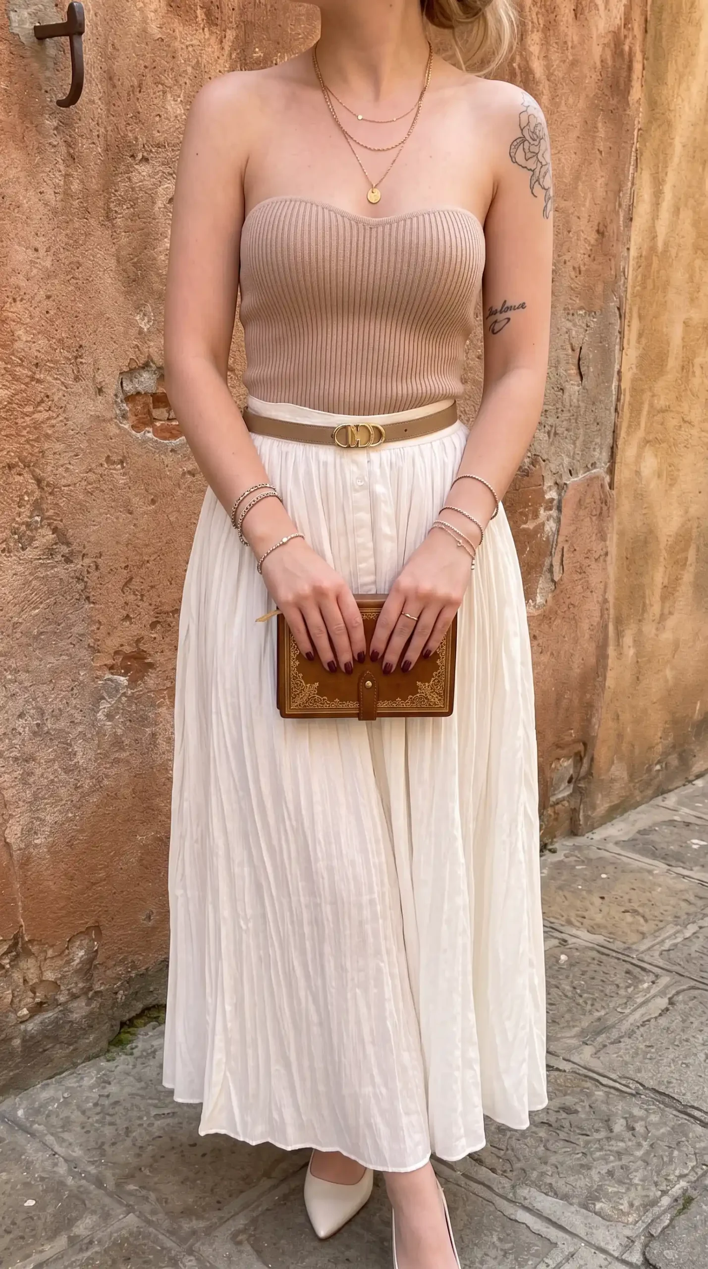 Woman wearing beige ribbed strapless tube top with cream pleated midi skirt and belt