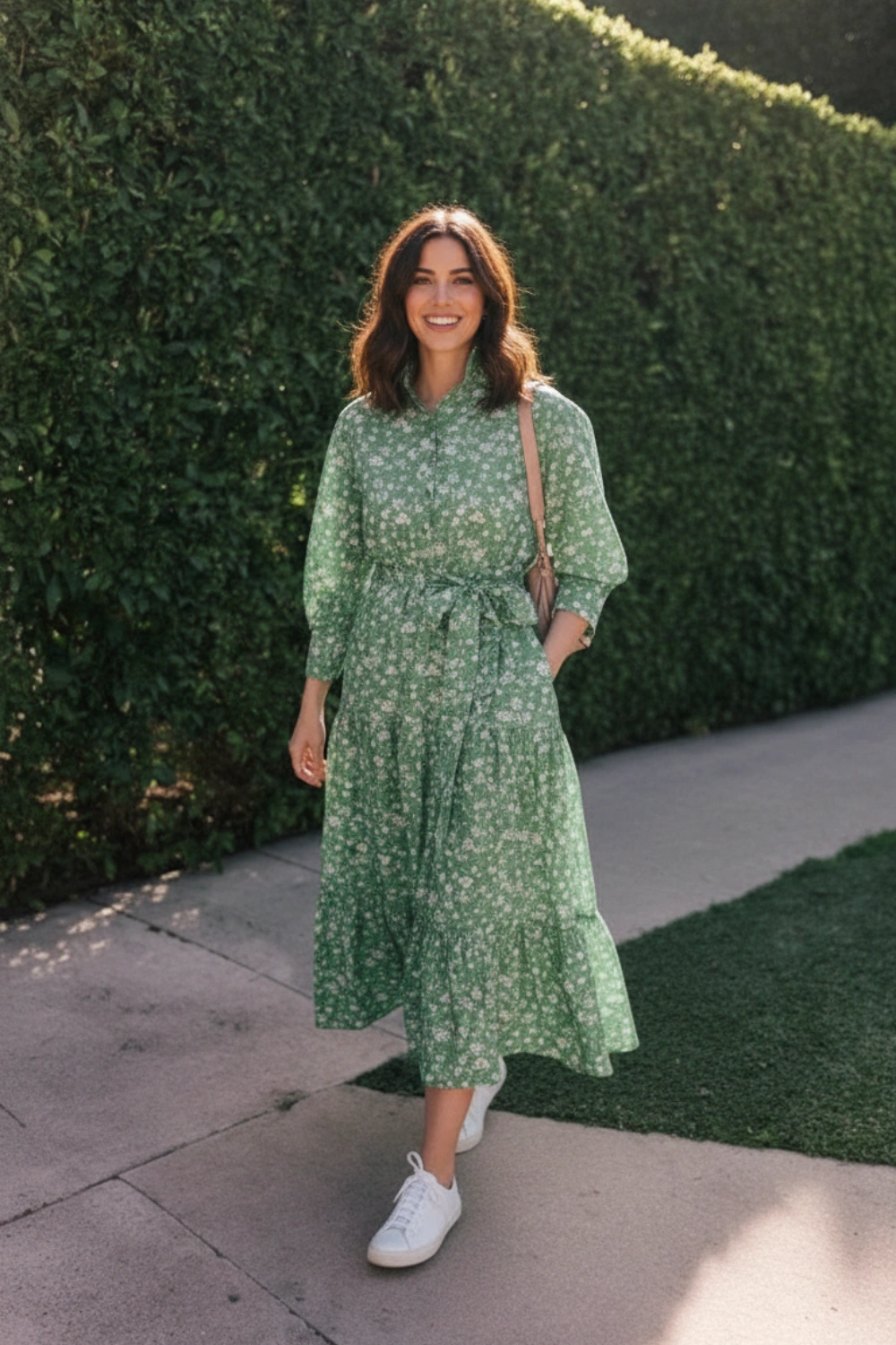 Woman wearing a long-sleeve green floral dress with white sneakers and a beige shoulder bag outdoors