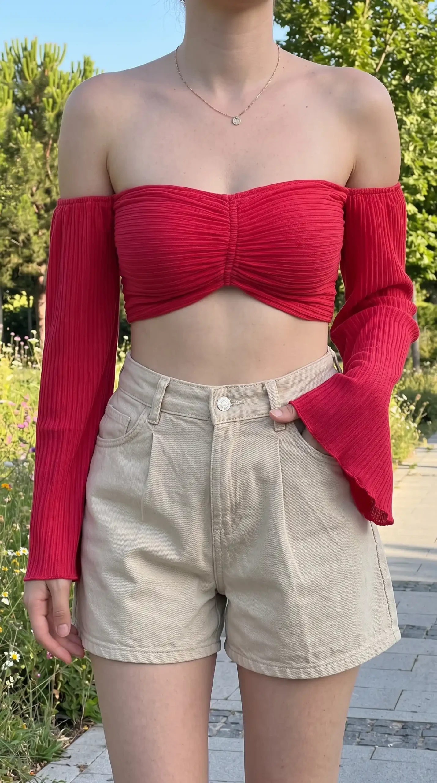 Woman wearing red off-shoulder crop top with bell sleeves and beige high-waisted shorts