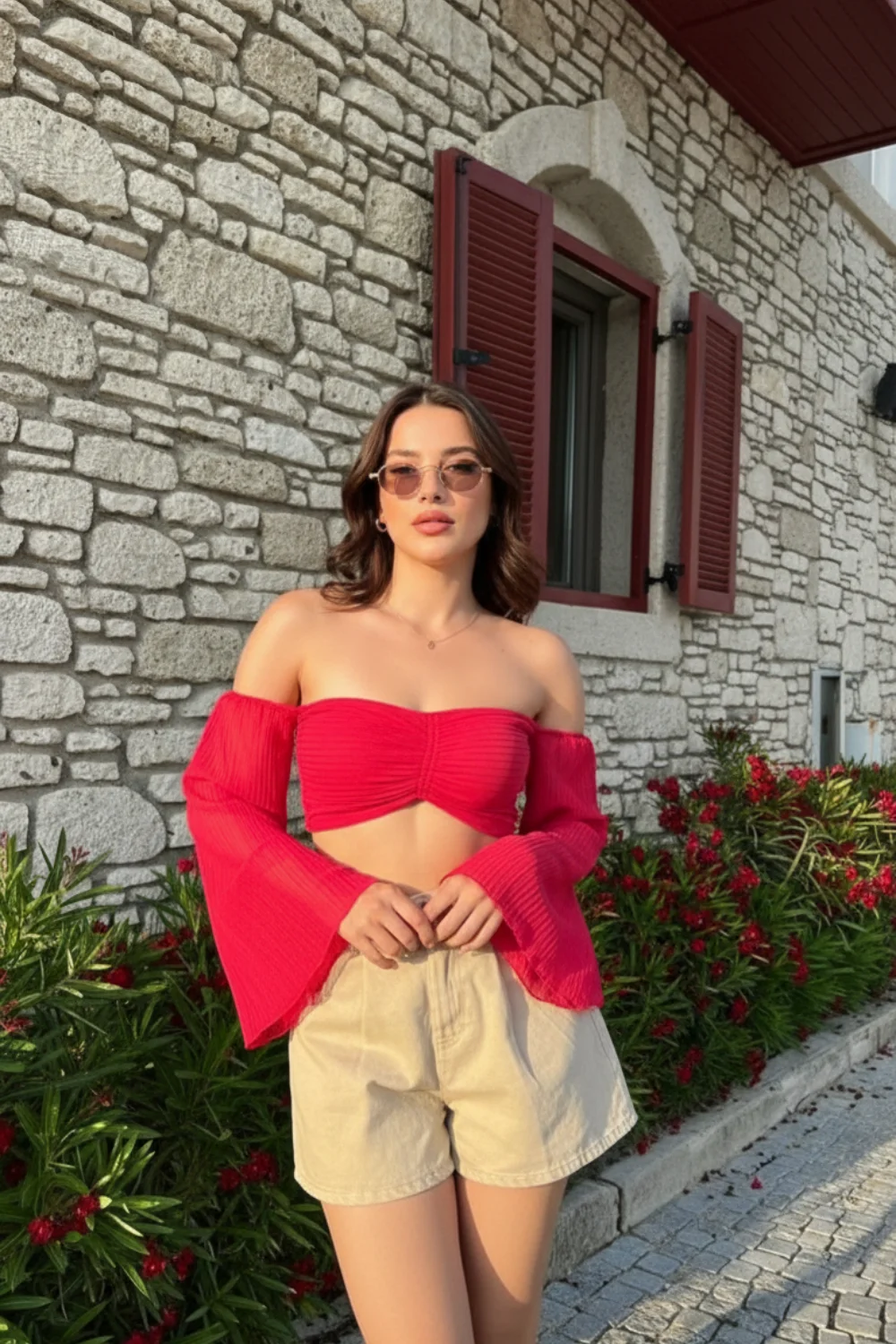 Woman wearing red off-shoulder crop top with bell sleeves and beige high-waisted shorts