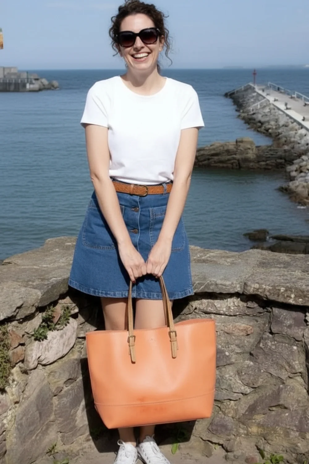 Woman wearing white t-shirt with denim button-front mini skirt and brown belt by the ocean
