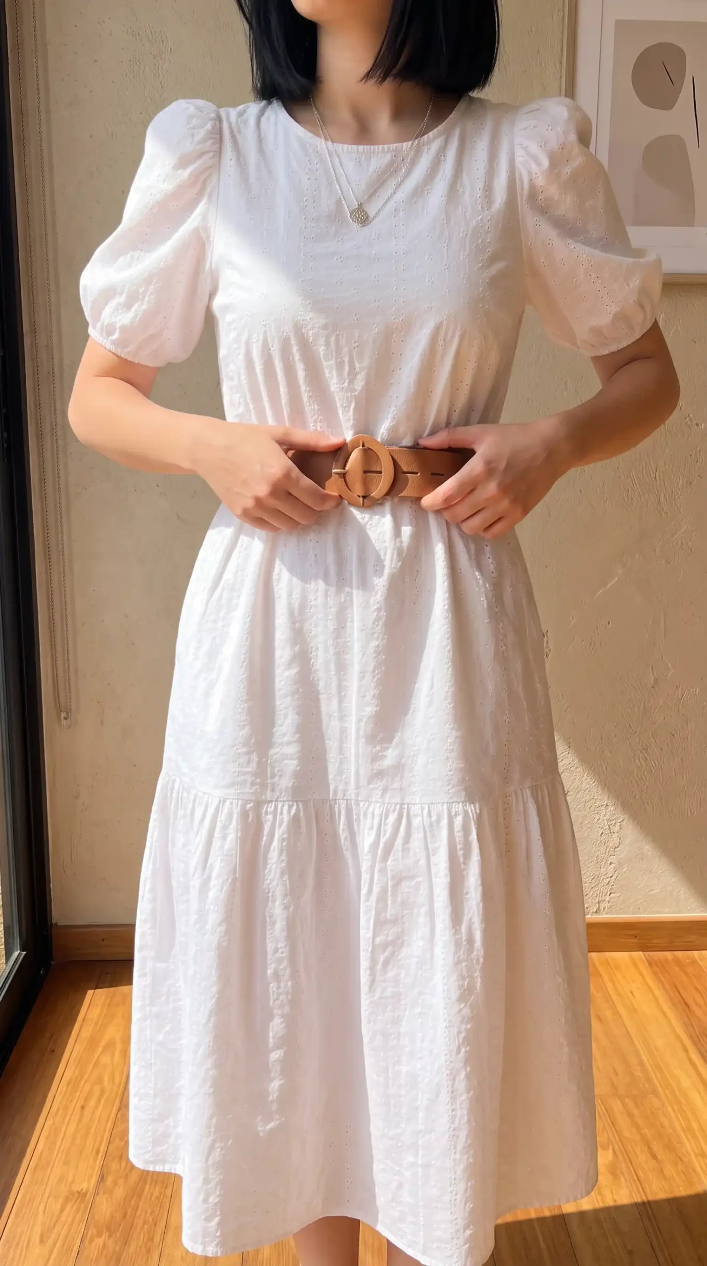 Woman wearing a white tiered midi dress with a brown belt and slip-on shoes outdoors