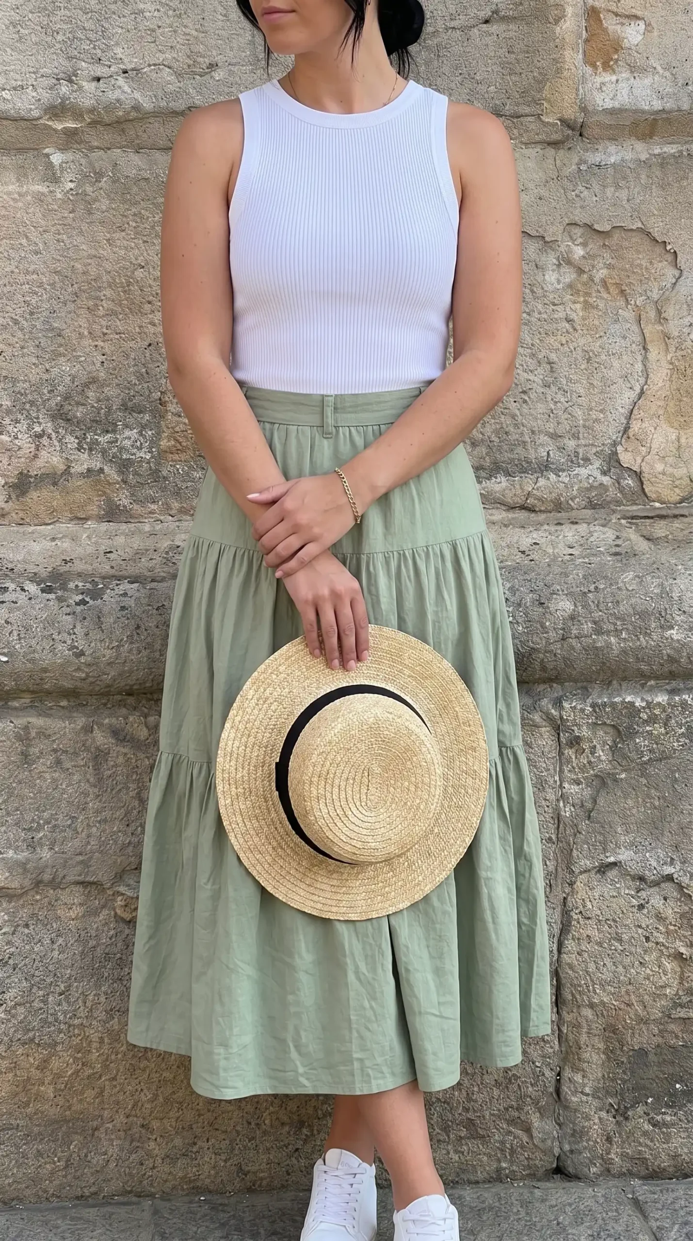Woman wearing a white sleeveless top with a light green tiered skirt and sneakers outdoors near the ocean