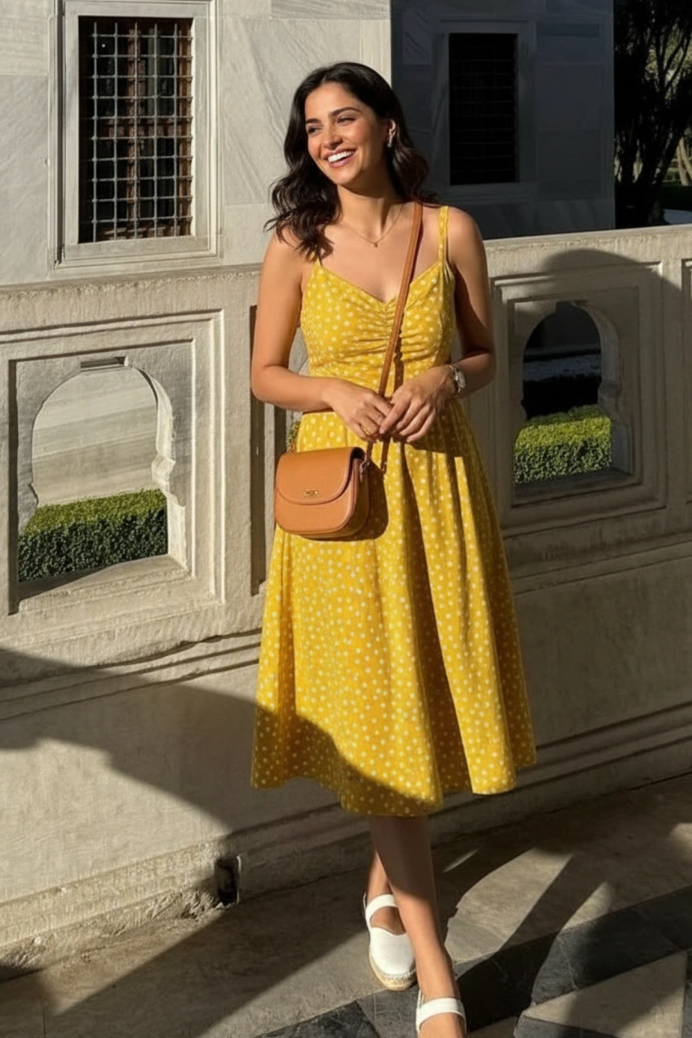 Woman wearing a yellow polka dot dress with white shoes and a brown crossbody purse outdoors