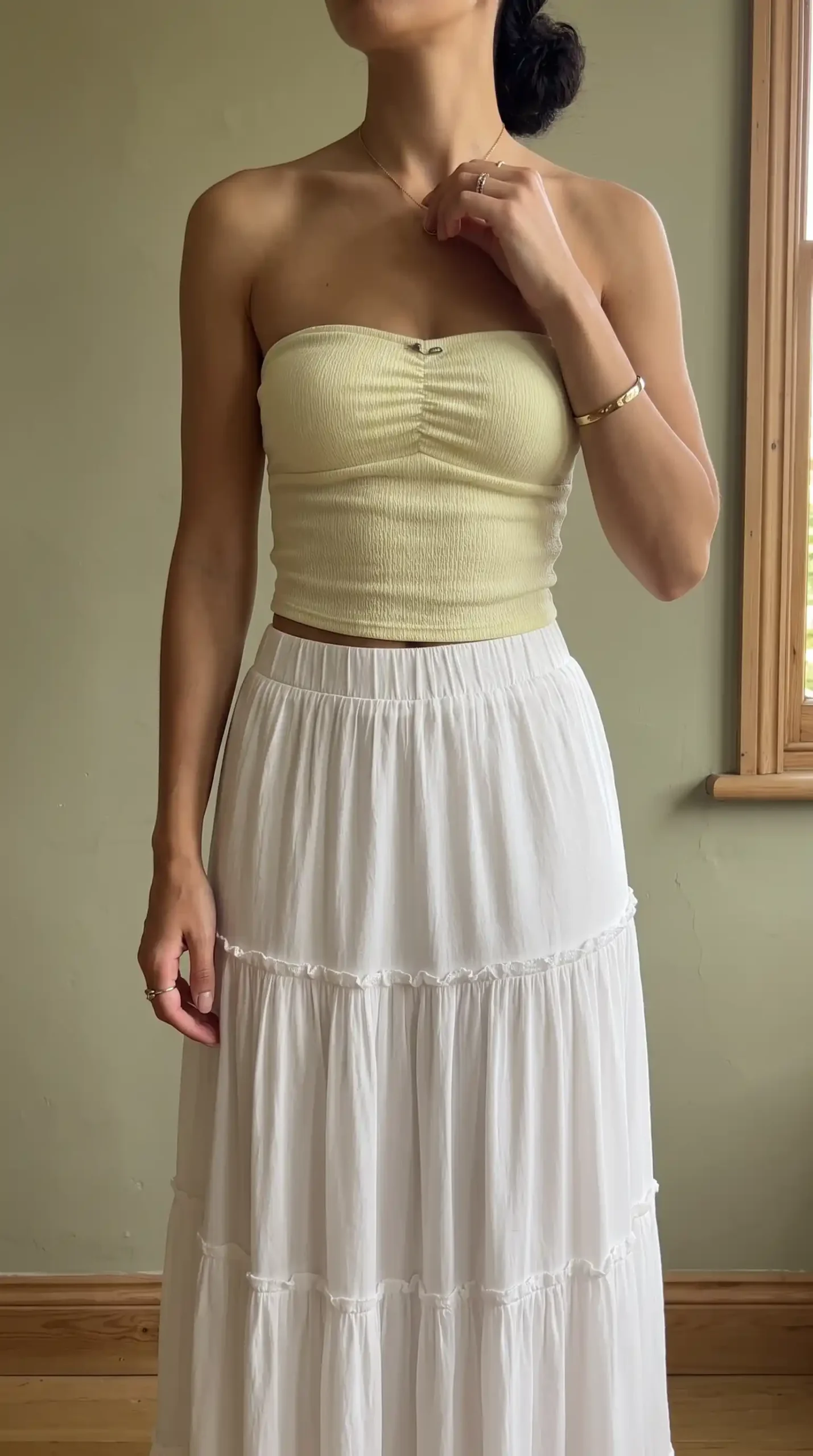 Woman wearing a light yellow strapless top with a white tiered skirt and brown handbag outdoors in the city