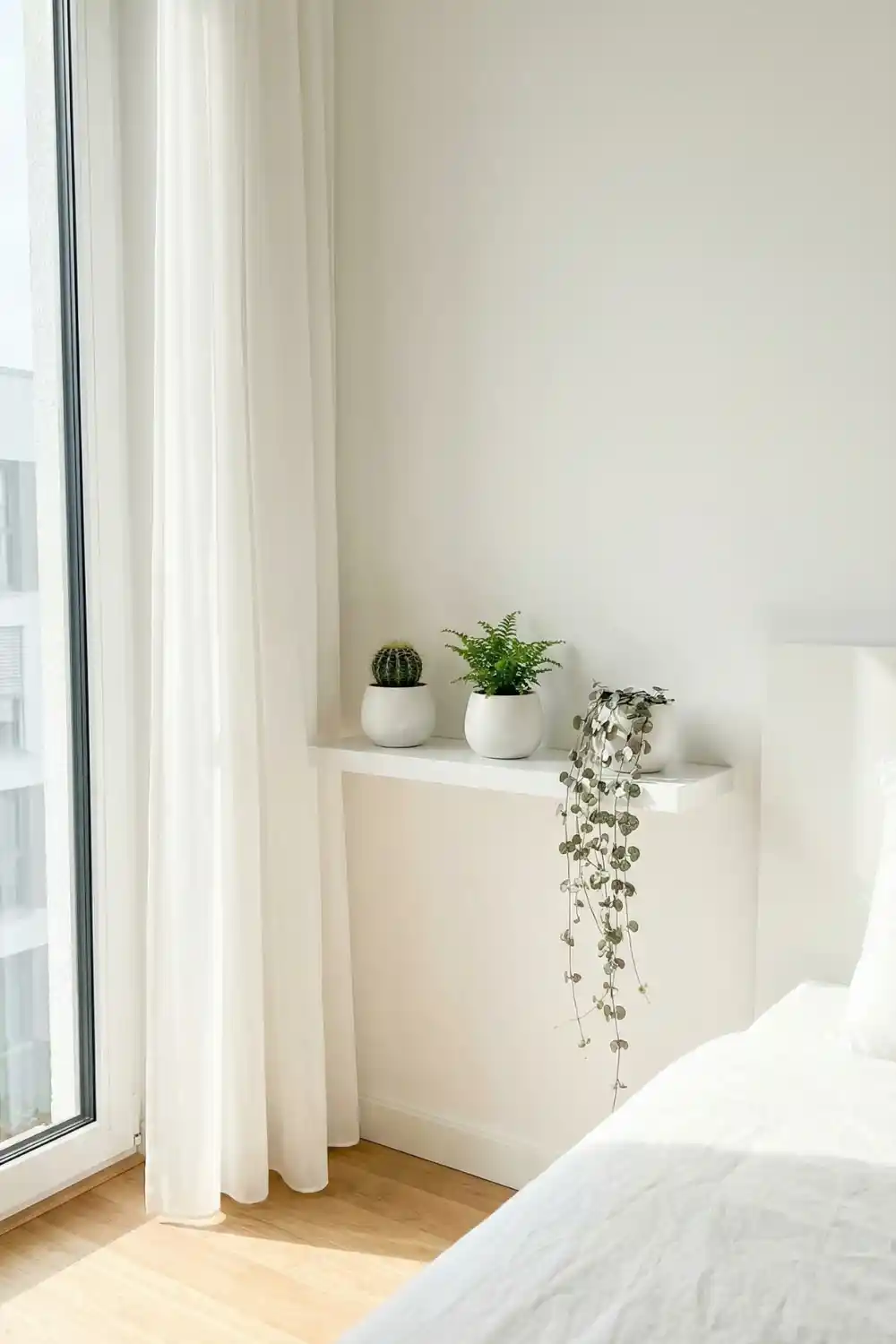 A slim white floating shelf mounted beside a bright window and styled with a small cactus, a tiny fern and a trailing string of hearts is the prettiest bedroom plant moment. This simple window plant shelf idea lets your plants soak up natural light while keeping your space feeling fresh and airy.