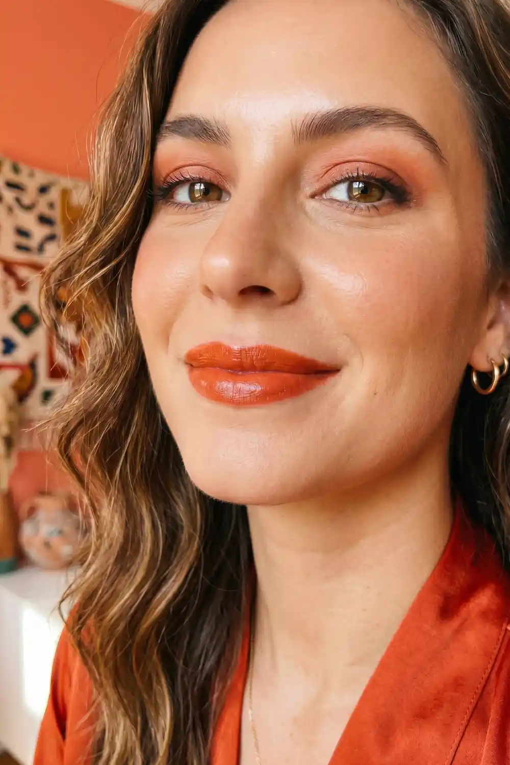 Woman wearing orange red warm glossy satin lipstick with vibrant bold makeup