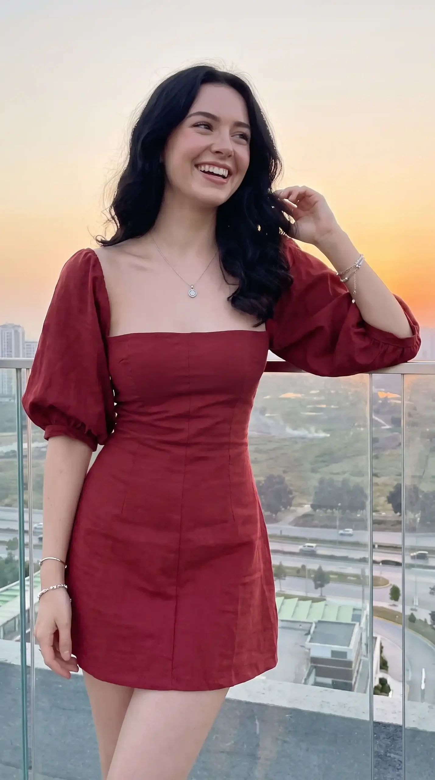 Woman wearing brick red linen square neck puff sleeve mini dress on balcony at sunset