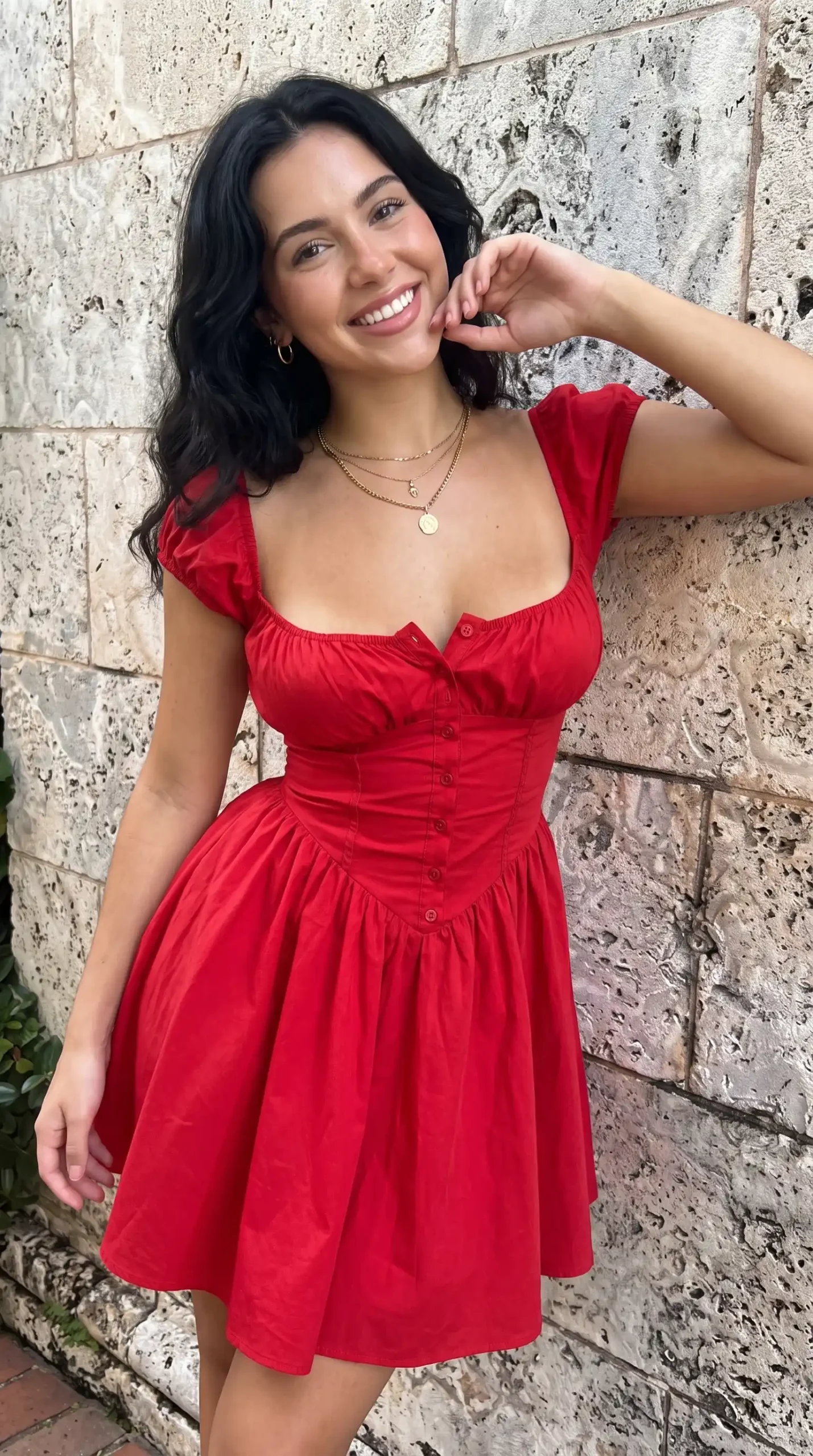 Woman wearing red button front corset skater mini dress against stone wall