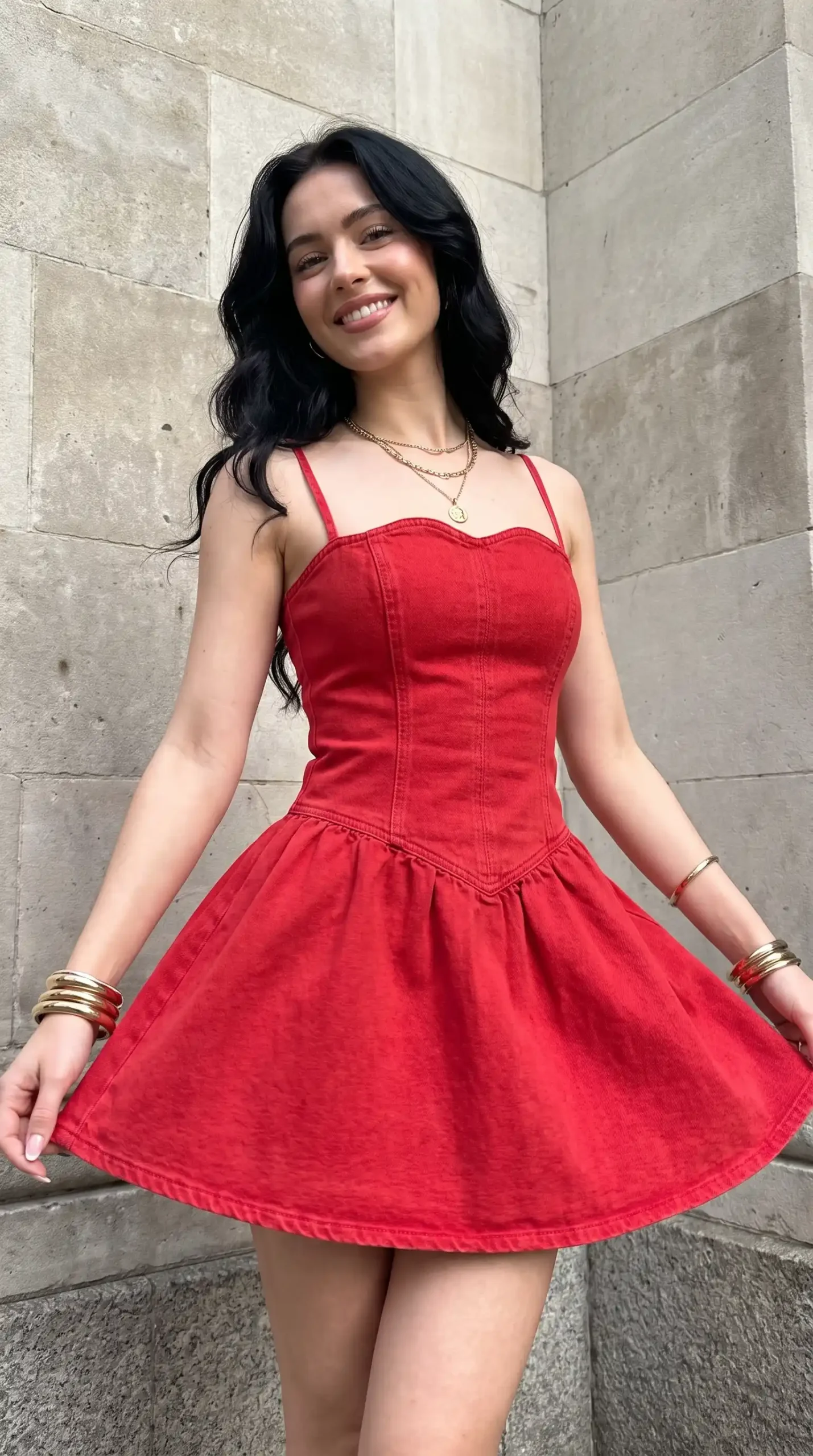 Woman wearing red denim sweetheart corset skater mini dress against stone wall