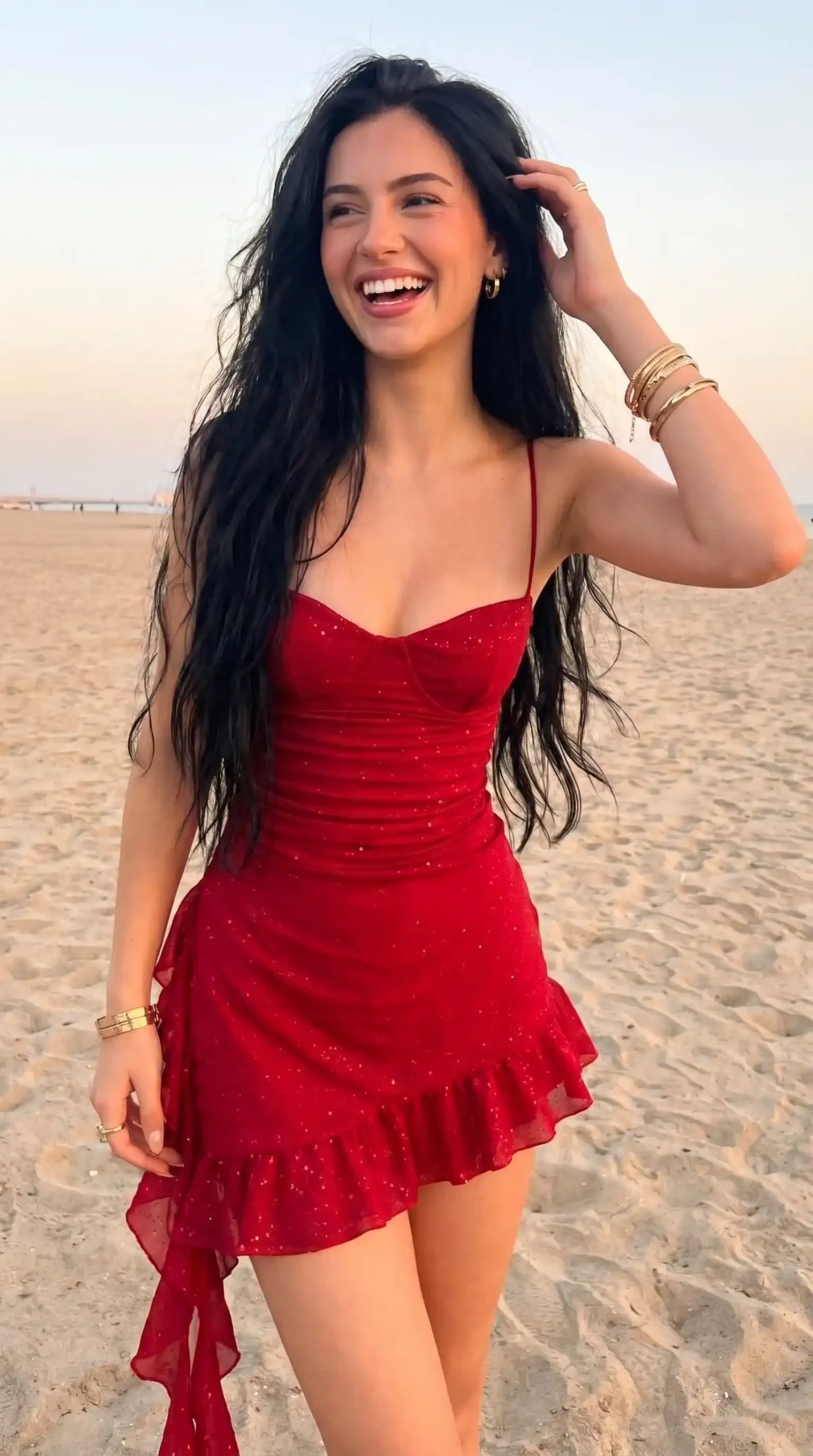 Woman wearing red glitter mesh bustier mini dress with asymmetric ruffle hem on beach