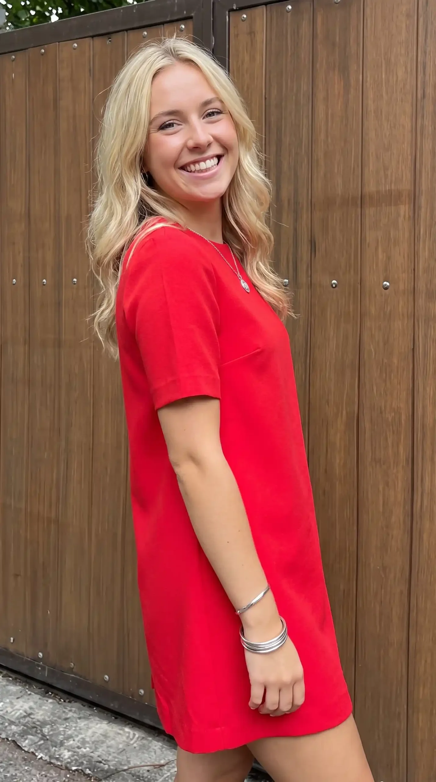Woman wearing red round neck short sleeve t-shirt mini dress against wooden fence