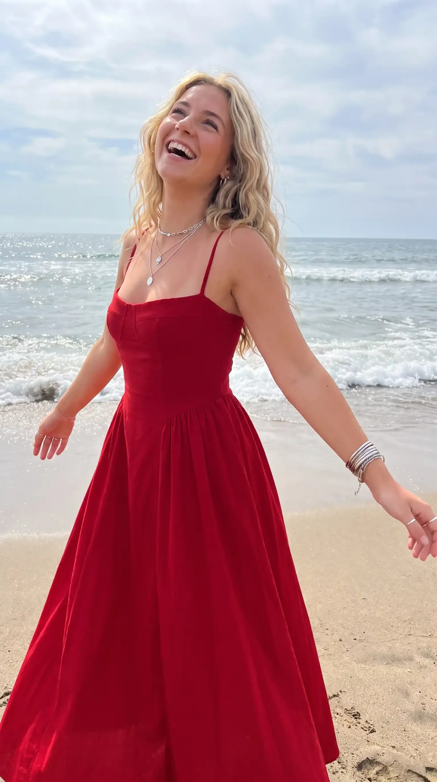 Woman laughing in red spaghetti strap maxi dress on the beach
