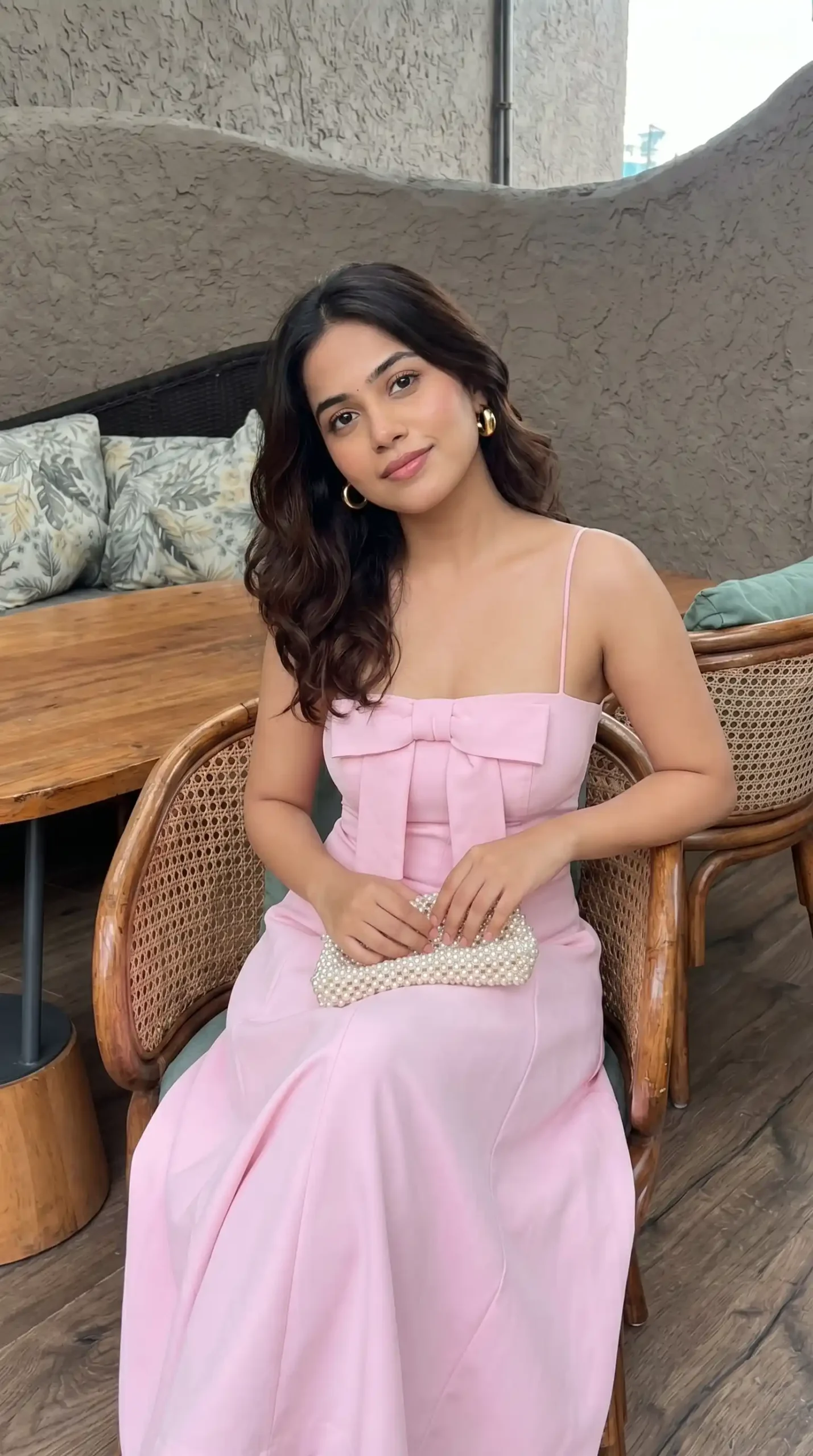 Woman wearing baby pink bow front strappy maxi dress with pearl clutch bag indoors