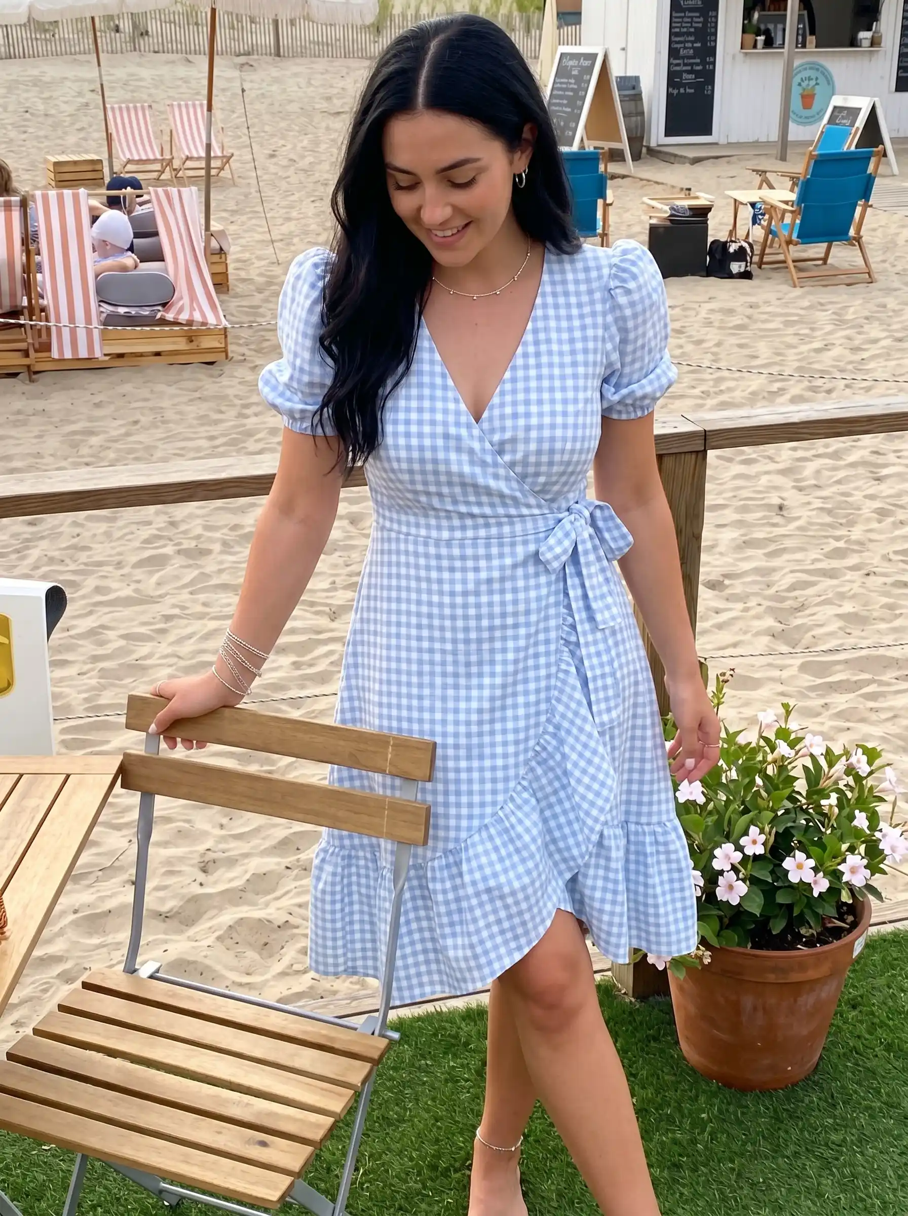 Woman wearing blue gingham puff sleeve wrap mini dress with ruffle hem at beach setting