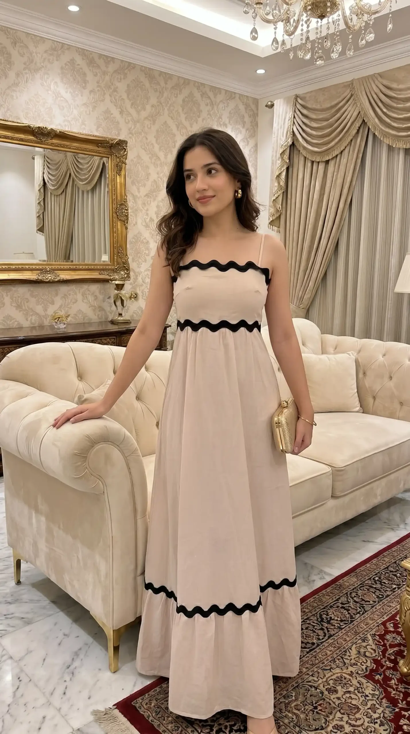 Woman wearing blush pink strappy maxi dress with black ric rac trim holding gold clutch indoors