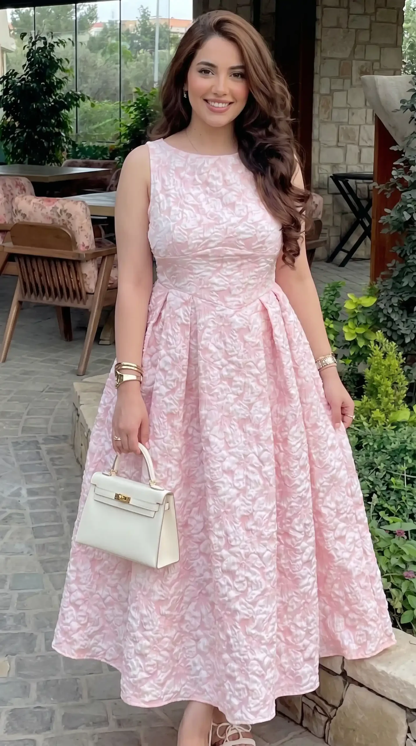Woman wearing blush pink floral jacquard sleeveless midi dress with white handbag in garden