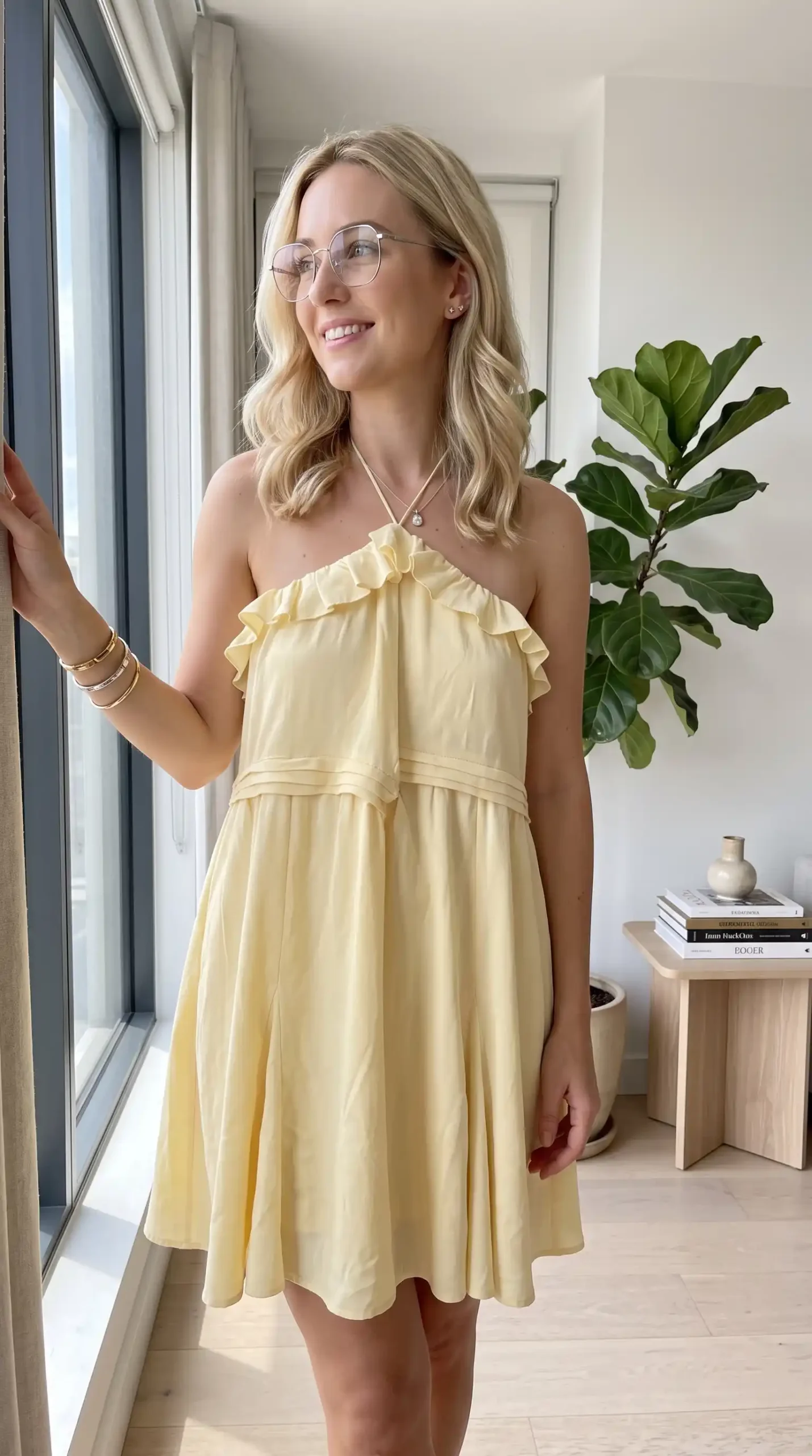 Woman wearing butter yellow halter neck ruffle mini dress with gold bangles and pearl necklace indoors