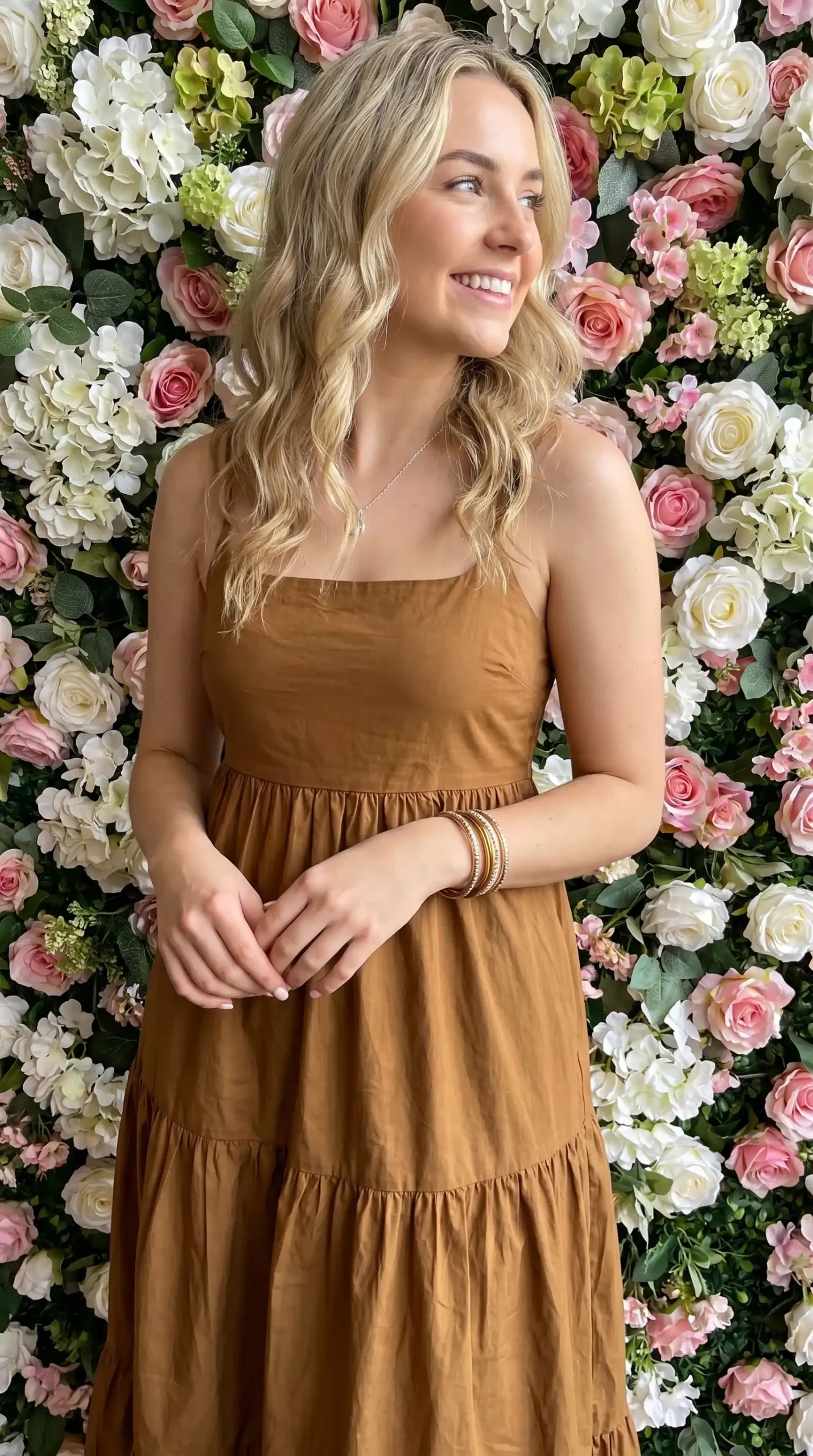 Woman wearing caramel brown strapless square neck tiered maxi dress in front of flower wall in summer