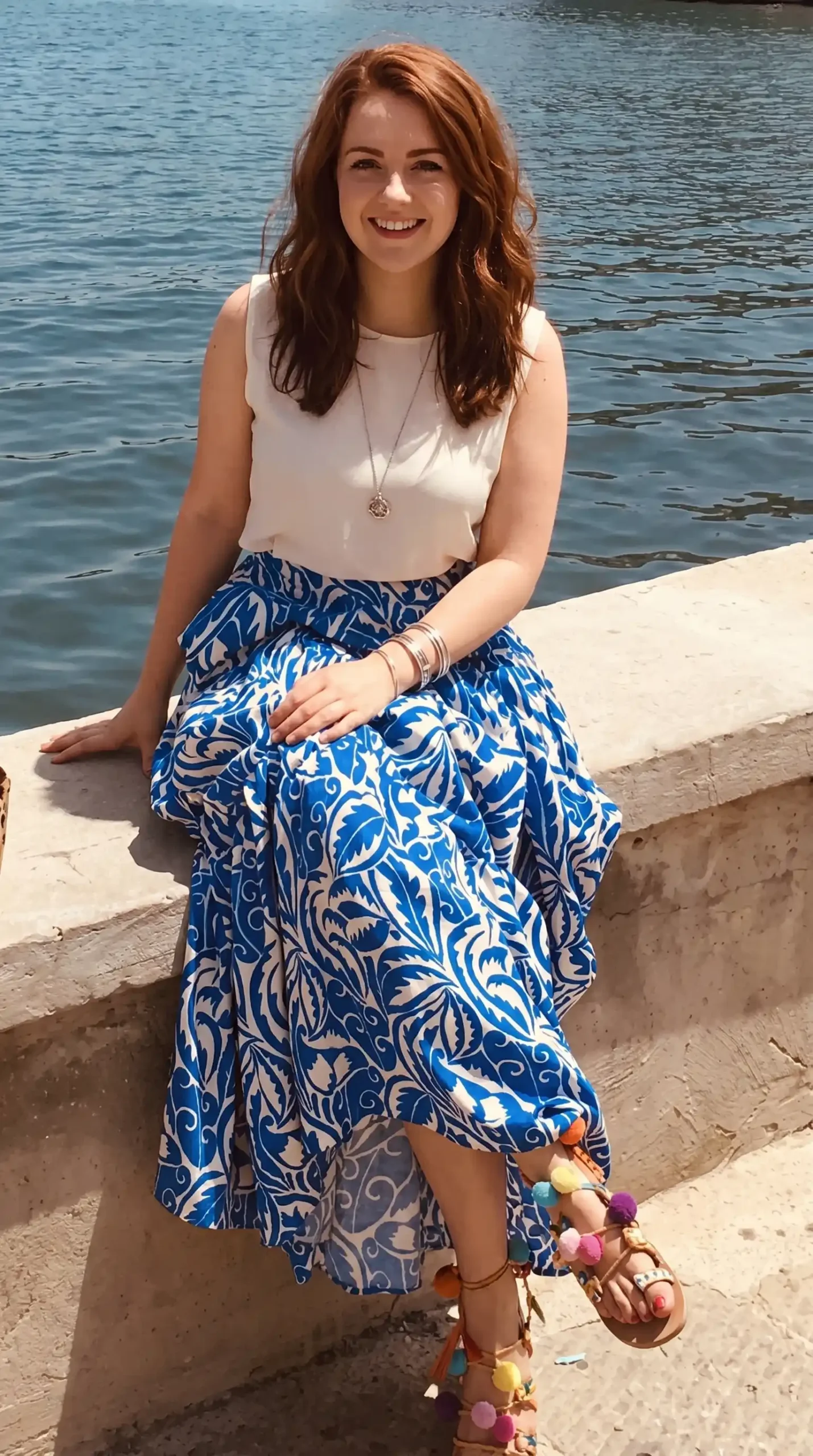 Woman wearing cobalt blue and white baroque print maxi skirt with white sleeveless top by waterfront