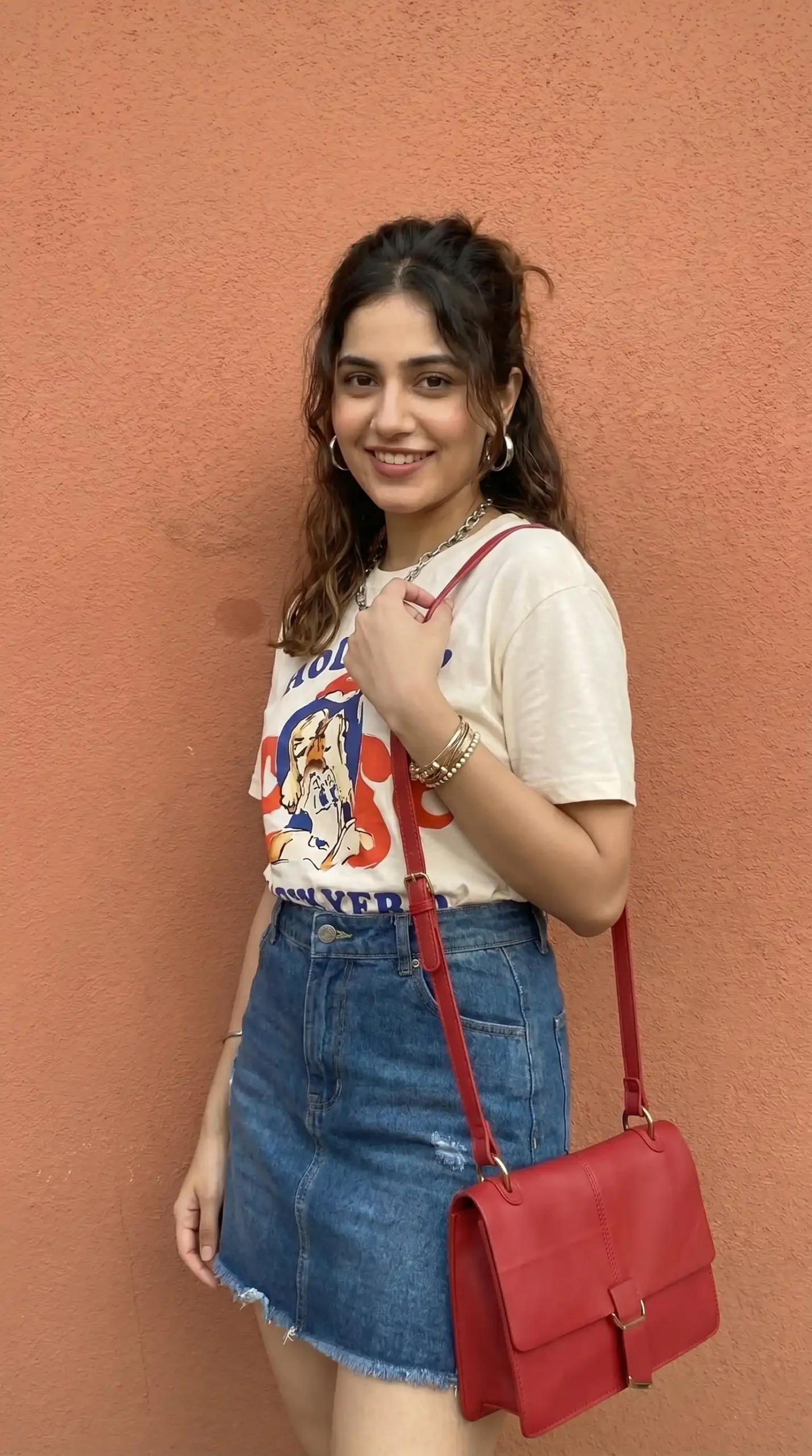 Woman wearing cream vintage graphic tee with dark denim mini skirt and red bag