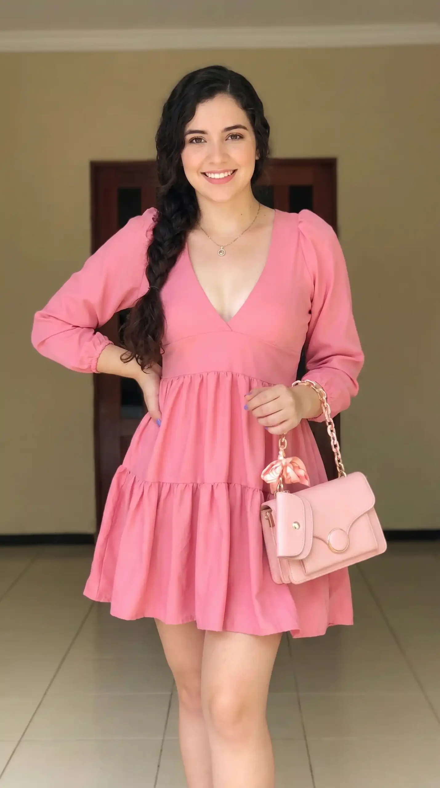 Woman wearing dusty rose pink V-neck long sleeve tiered mini dress with light pink chain bag