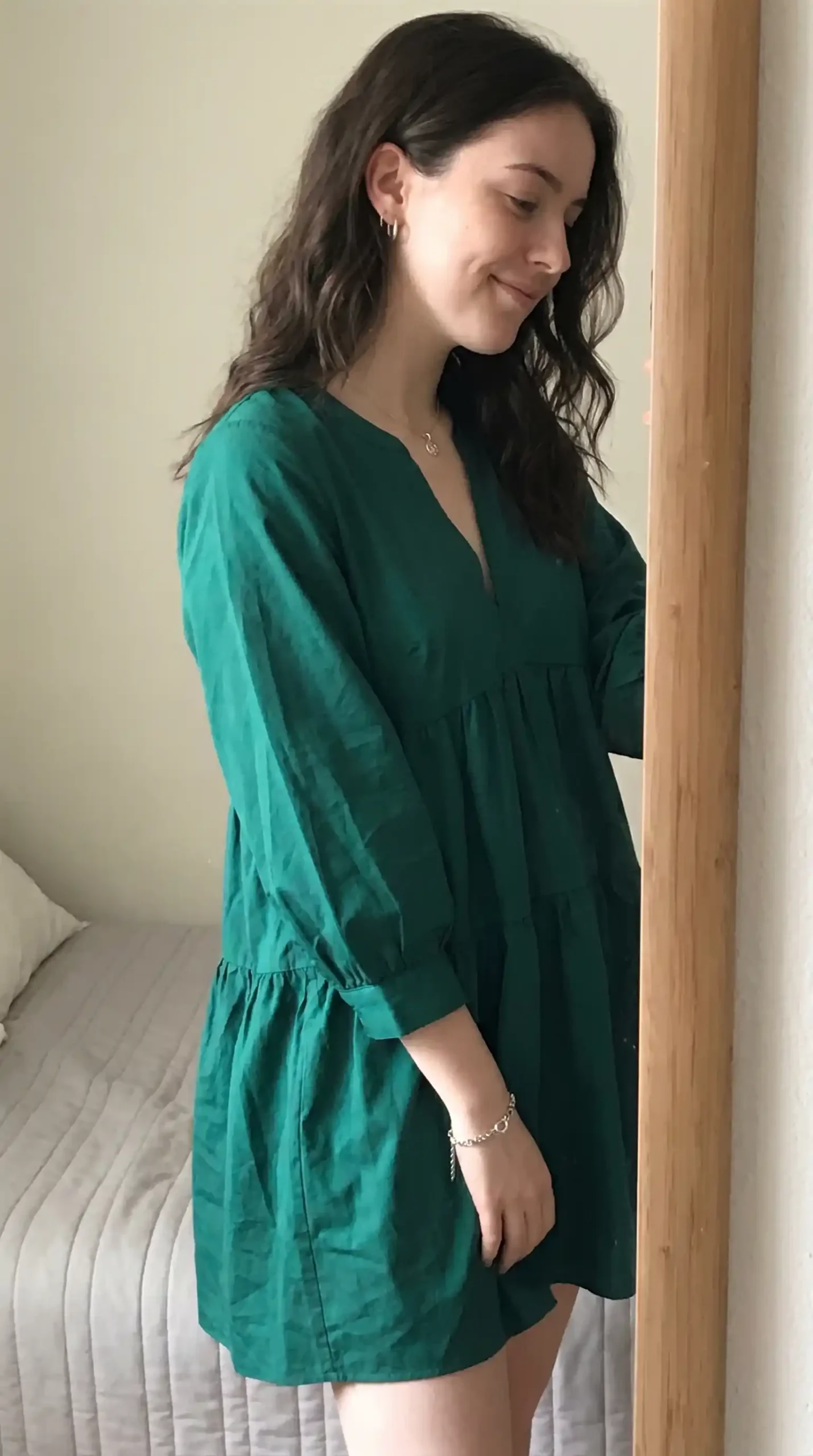 Woman wearing emerald green V-neck tiered babydoll mini dress indoors by mirror