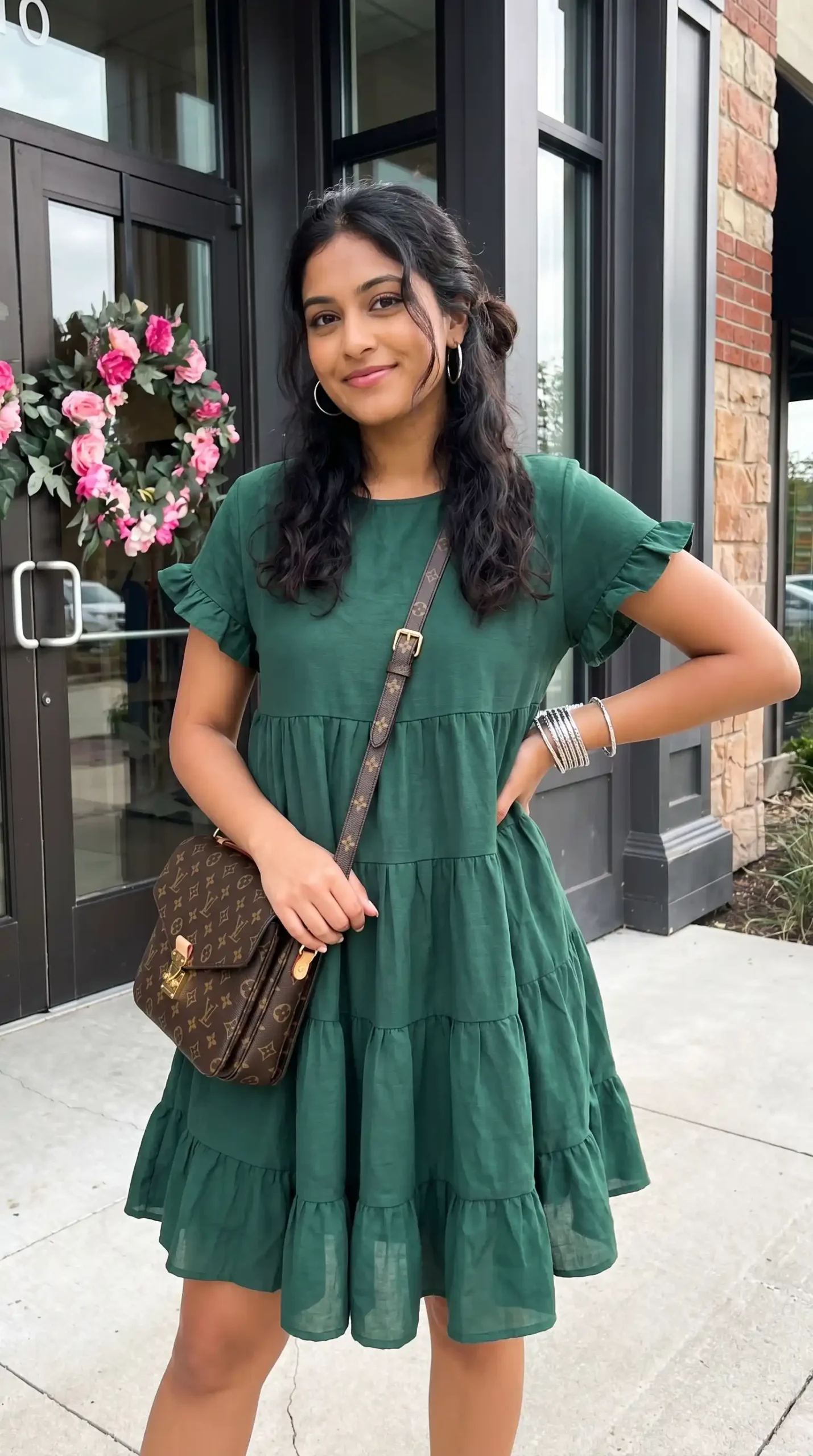 Woman wearing forest green ruffle sleeve tiered mini dress with brown crossbody bag outdoors