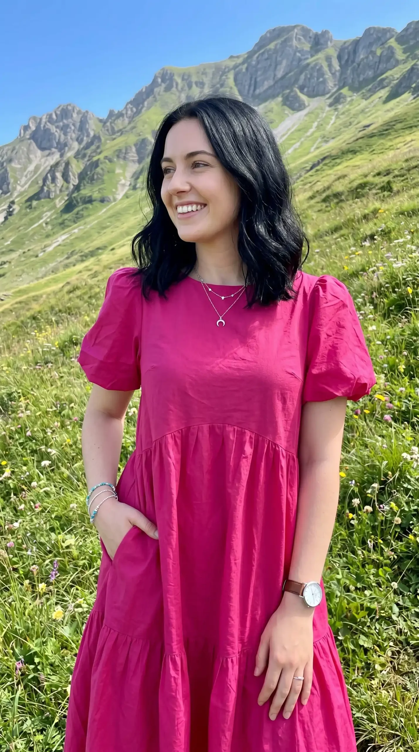 Woman wearing fuchsia pink puff sleeve round neck tiered maxi dress in mountain meadow in summer