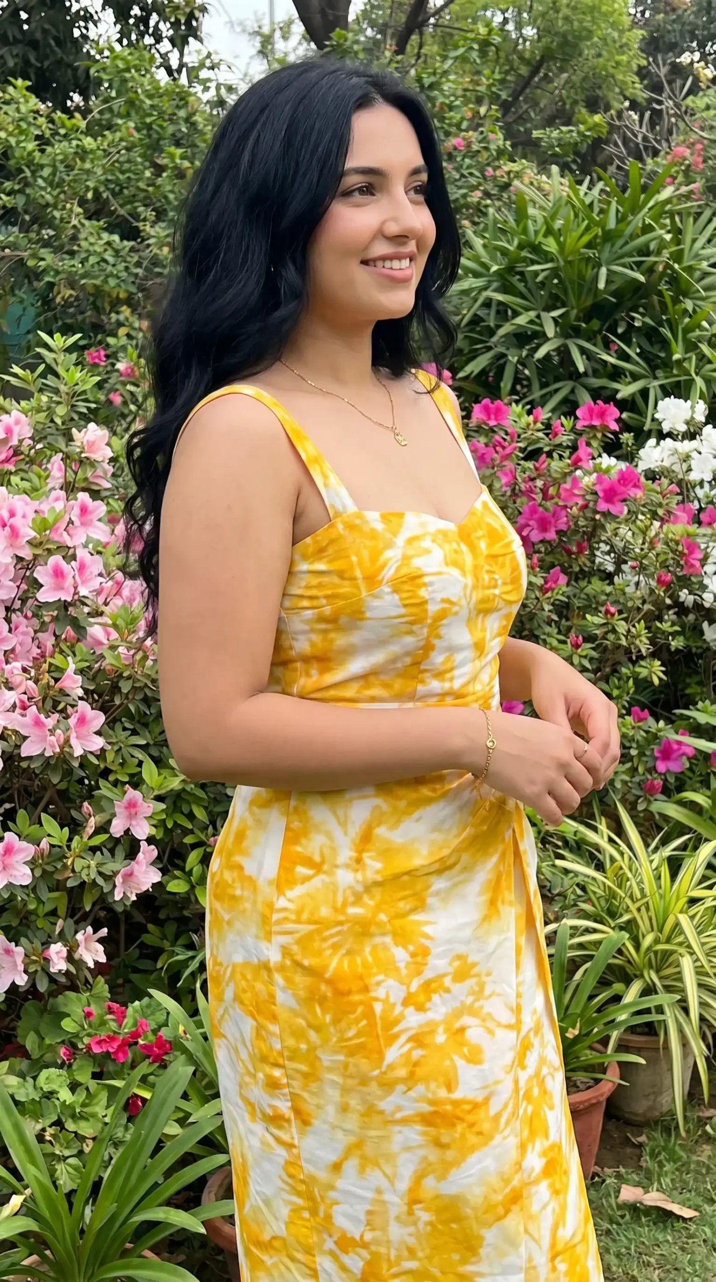 Woman wearing golden yellow and white tie dye spaghetti strap midi dress in flower garden in summer