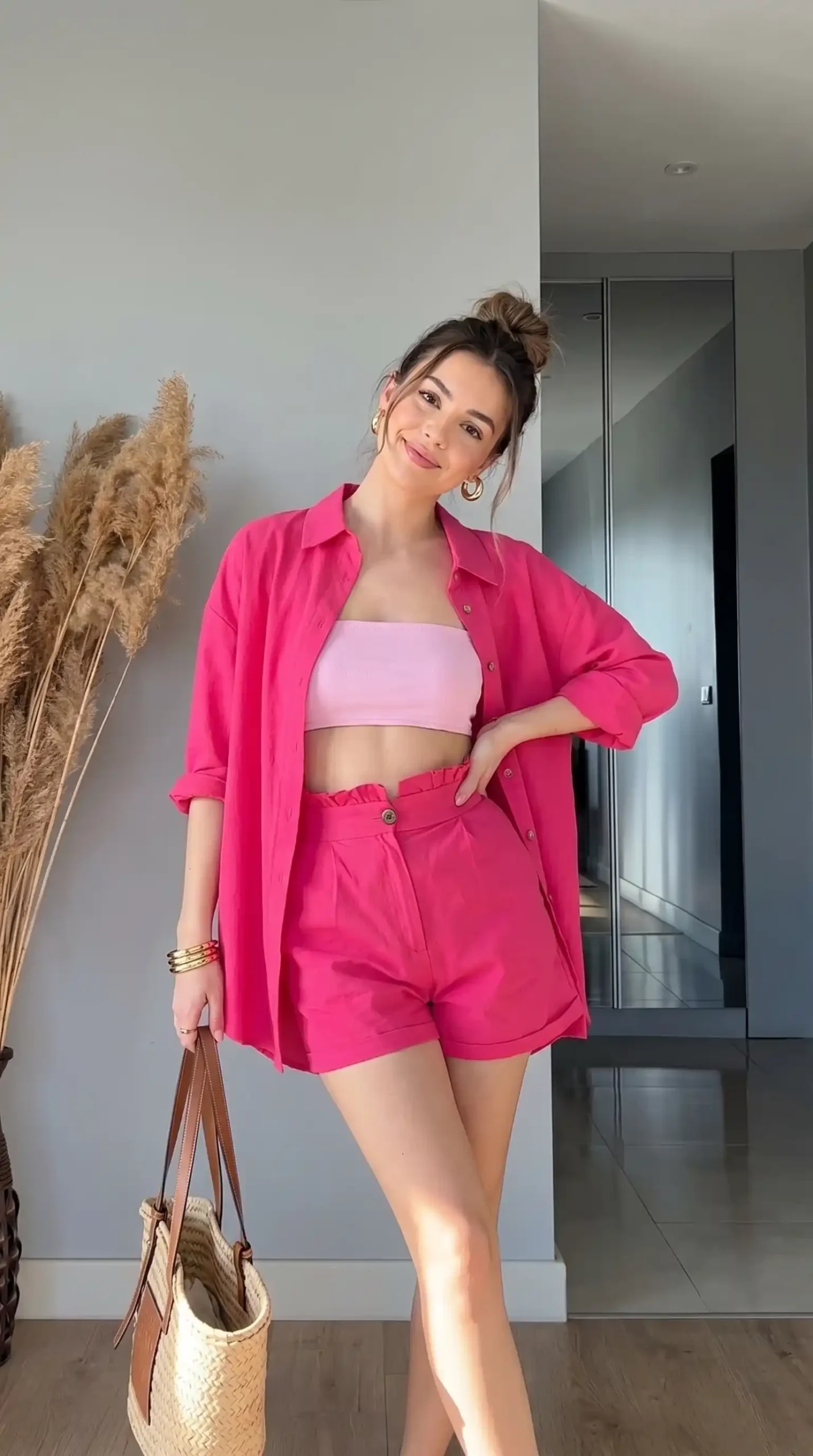 Woman wearing hot pink oversized shirt and matching shorts co-ord set with light pink bandeau and straw bag