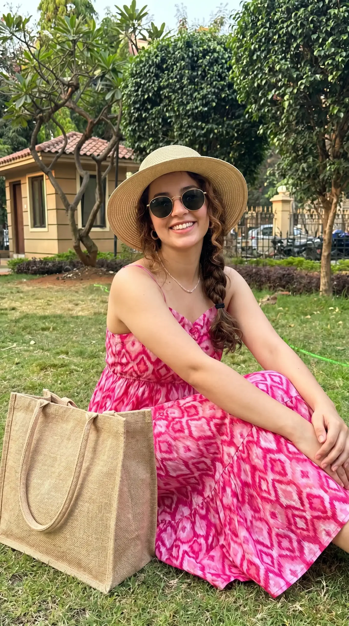 Woman wearing hot pink ikat print strappy midi dress with straw hat and jute tote bag in garden