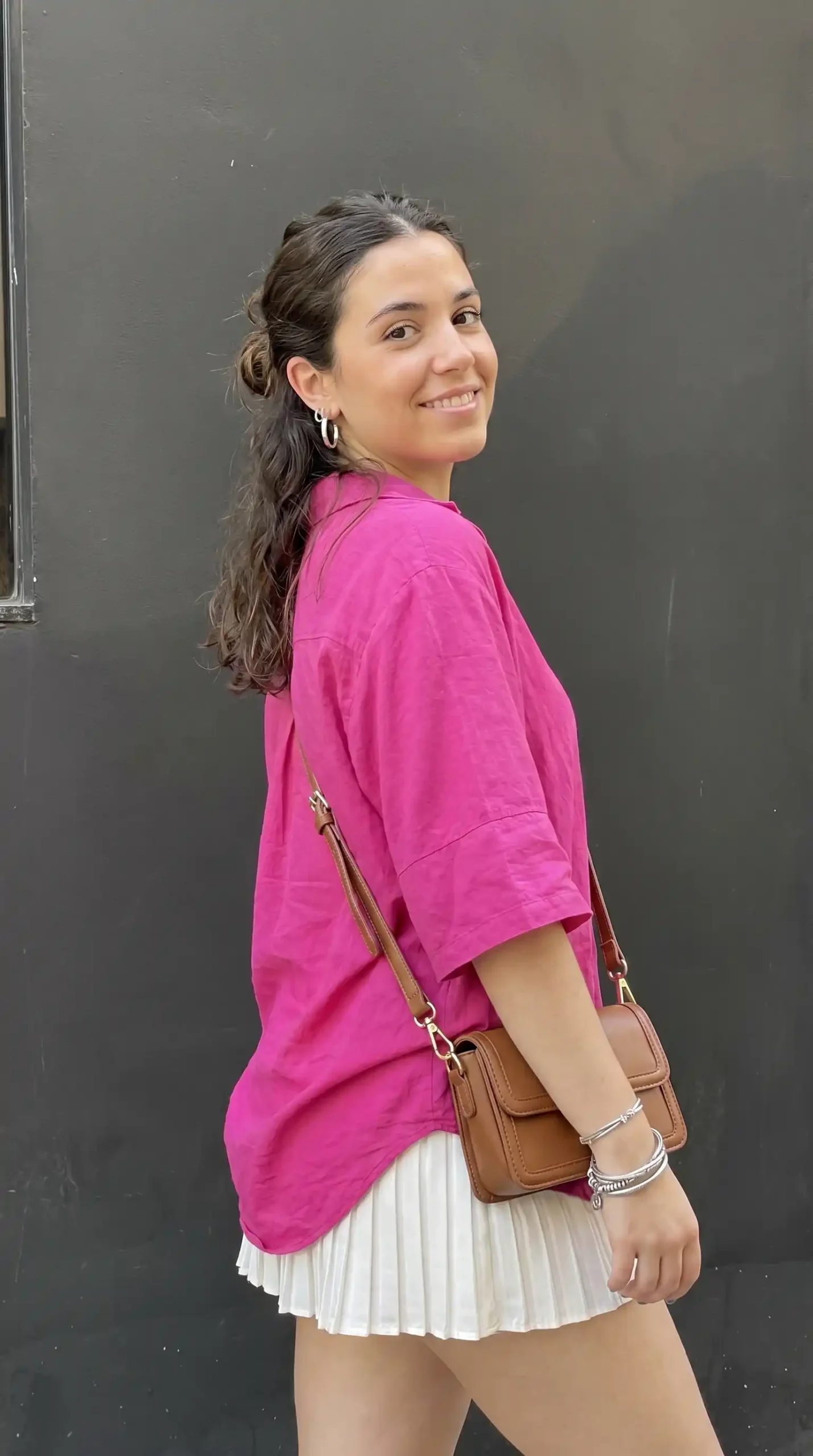 Woman wearing hot pink t-shirt with white pleated mini skirt and brown bag