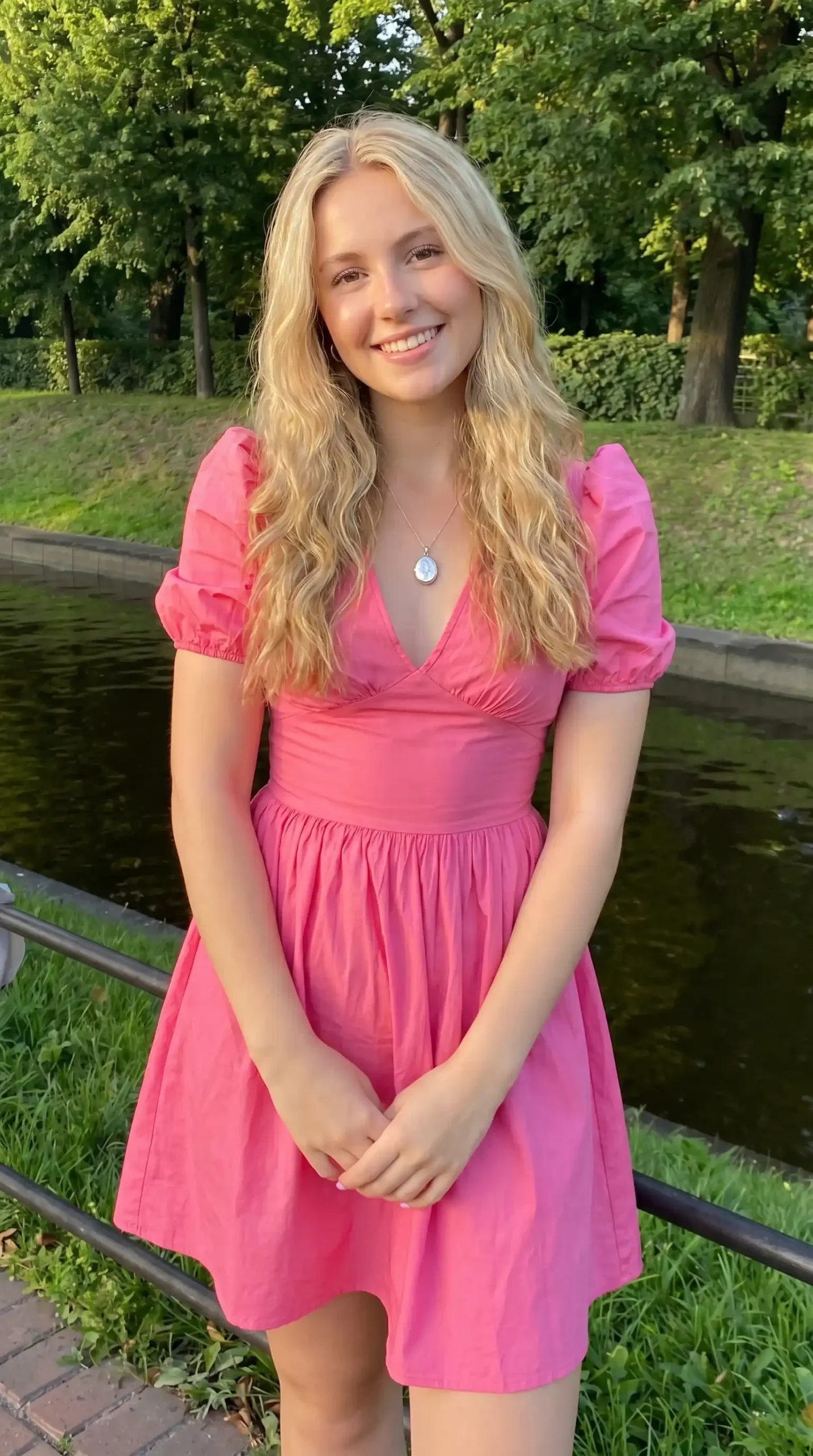Woman wearing hot pink puff sleeve V-neck babydoll mini dress in park by water in summer