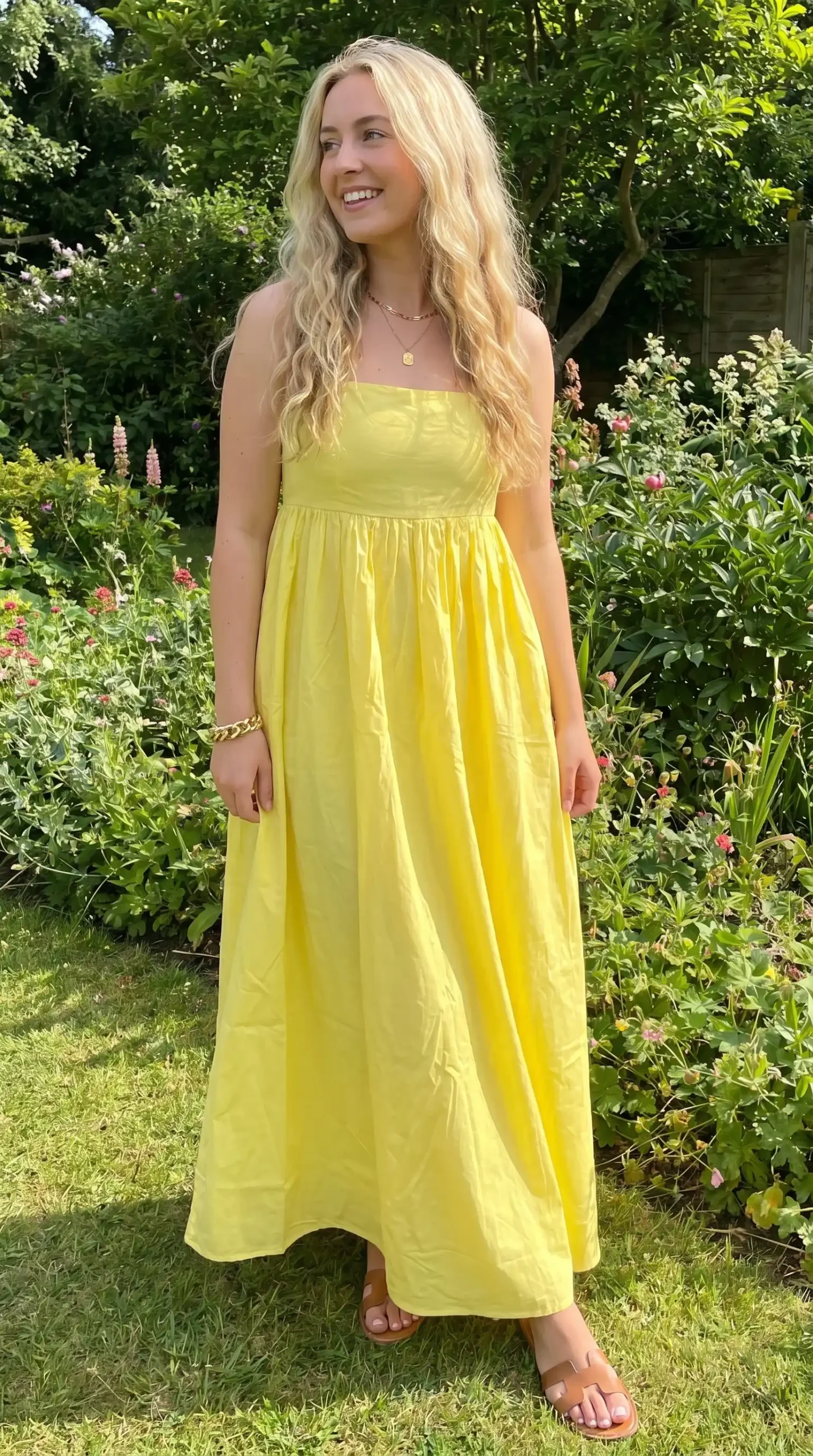 Woman wearing lemon yellow strapless square neck maxi dress in garden with flowers in summer