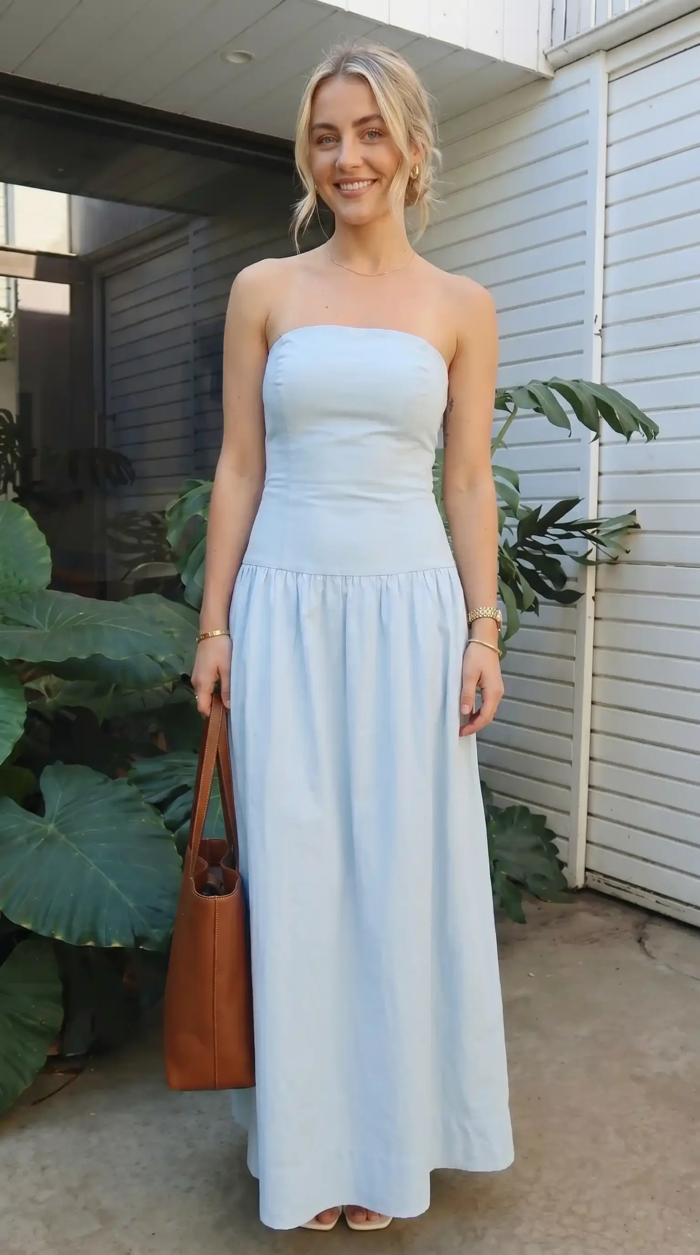 Woman wearing light blue strapless maxi dress with drop waist and brown leather tote bag