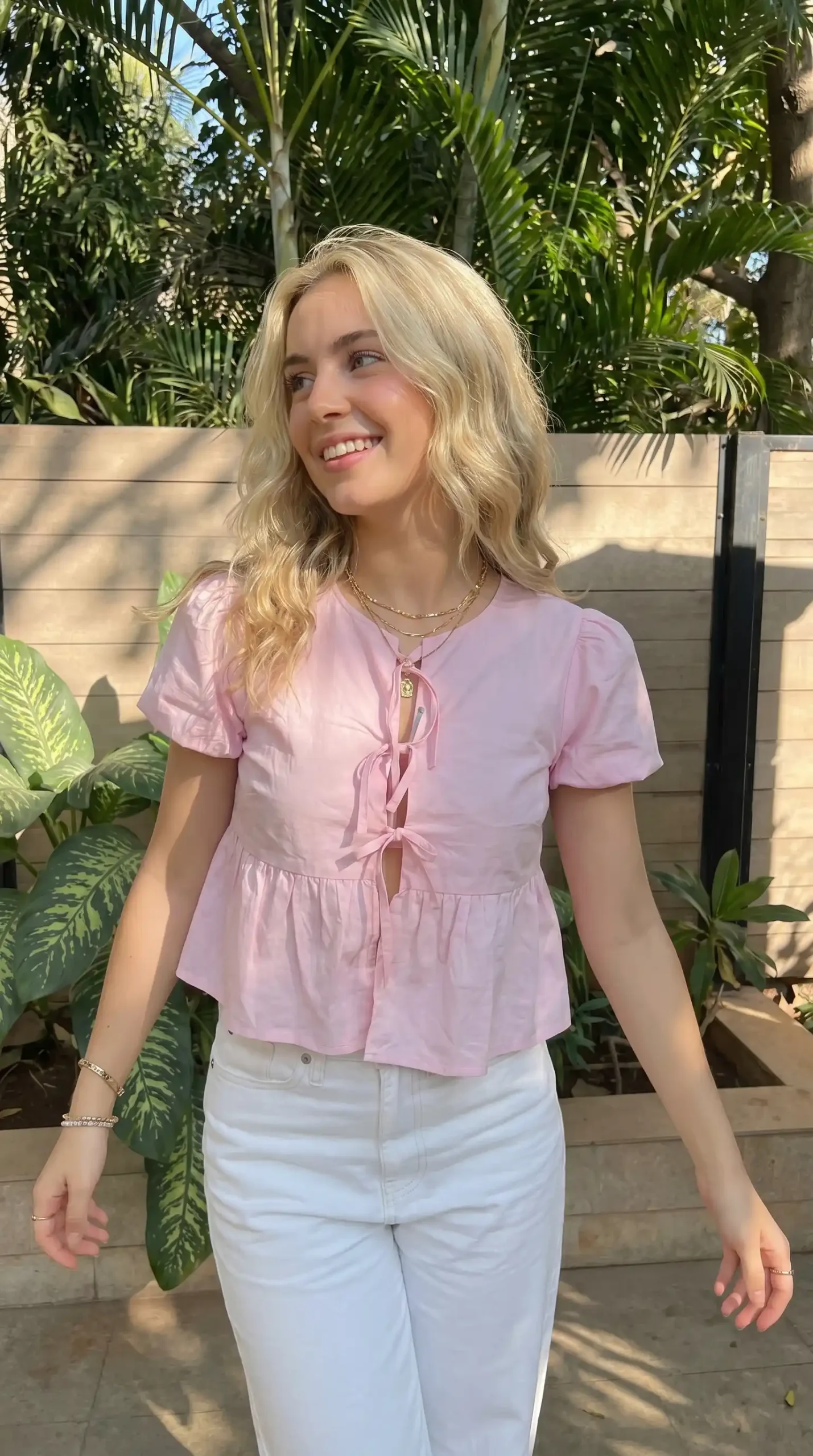 Woman wearing light pink tie front puff sleeve peplum crop top with white jeans outdoors in summer