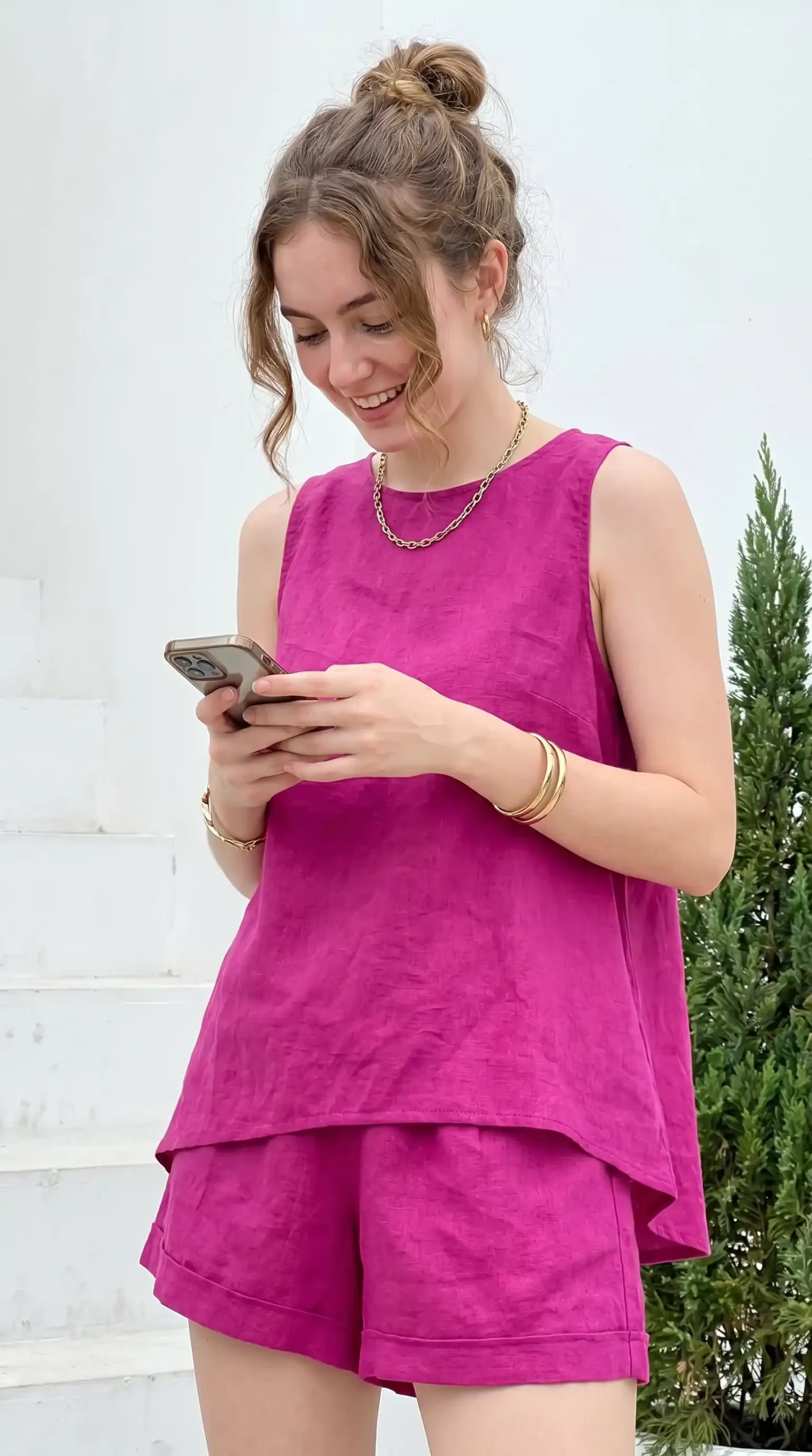 Woman wearing magenta sleeveless tank top with magenta shorts against white wall