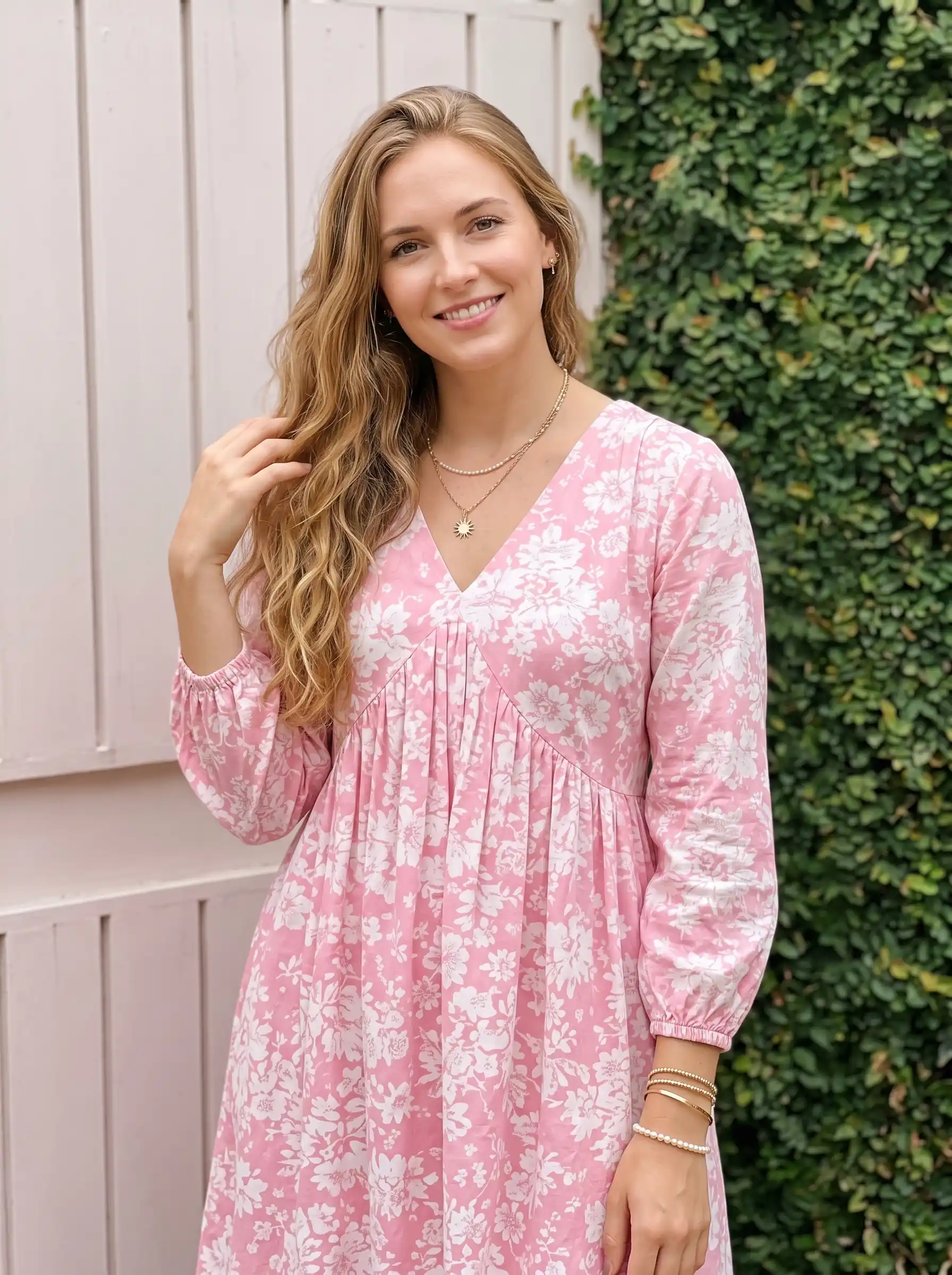 Woman wearing pink and white floral v-neck long sleeve midi dress with gold layered necklaces outdoors