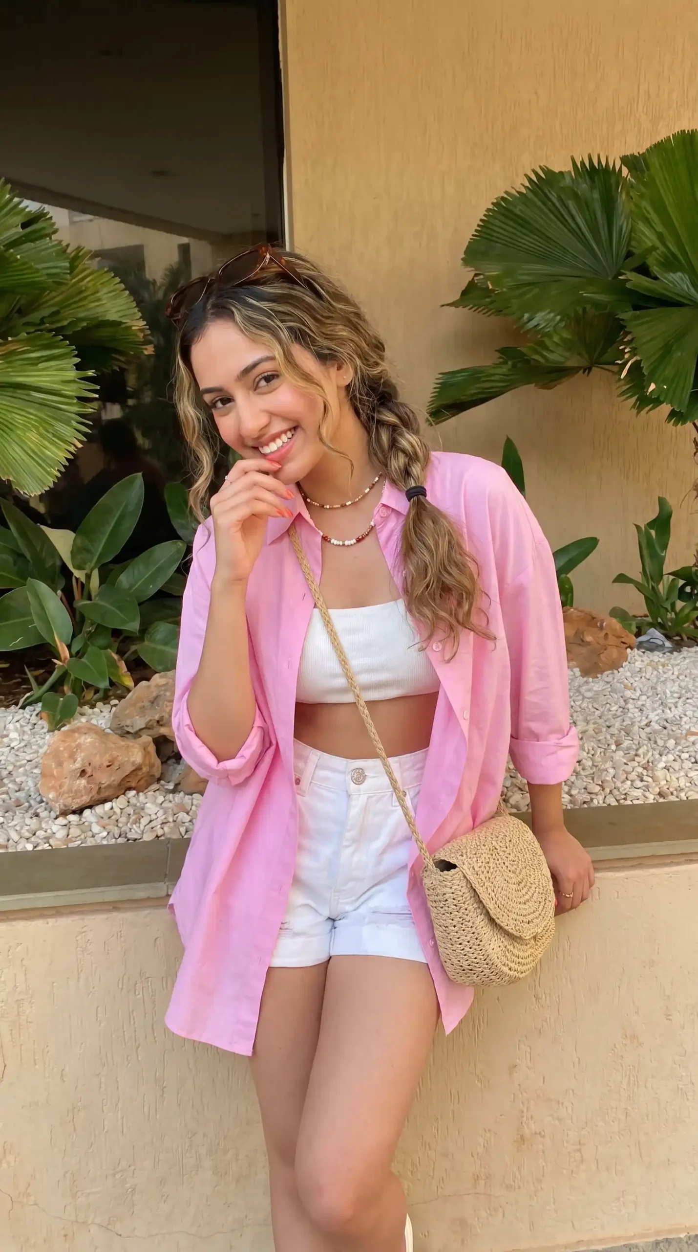 Woman wearing pink oversized shirt with white bandeau top and white denim shorts with straw bag outdoors