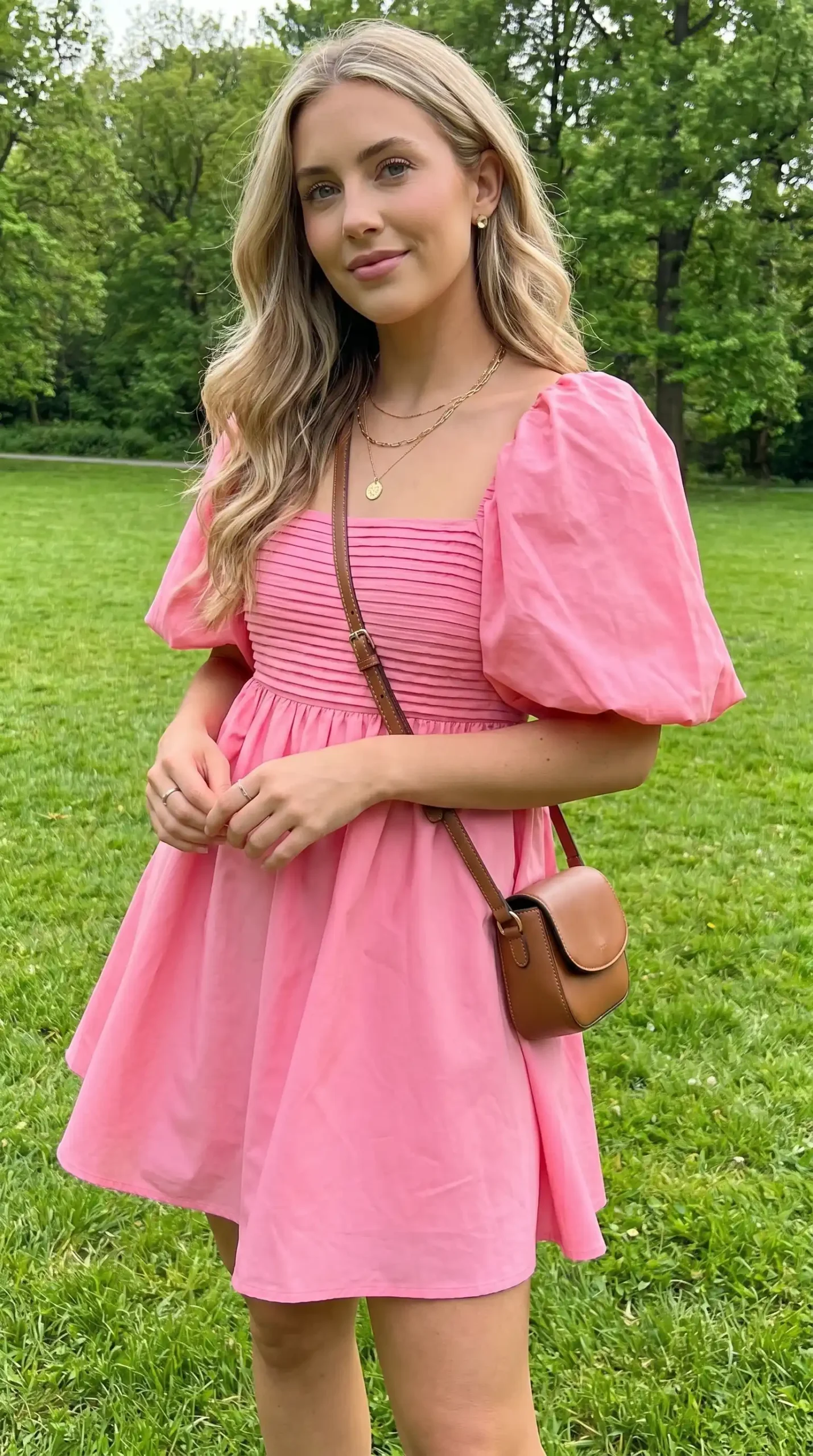 Woman wearing pink puff sleeve square neck babydoll mini dress with brown crossbody bag in park