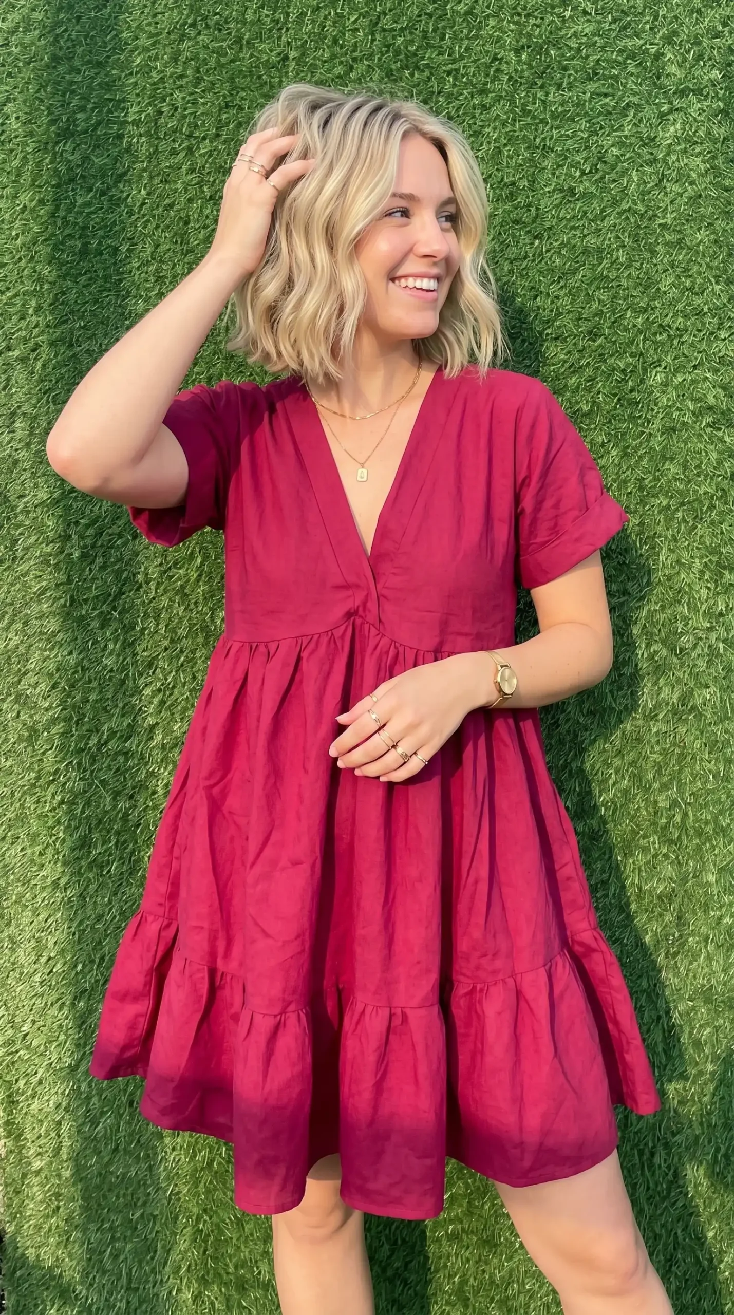 Woman wearing raspberry pink deep V neck short sleeve tiered babydoll mini dress outdoors in summer