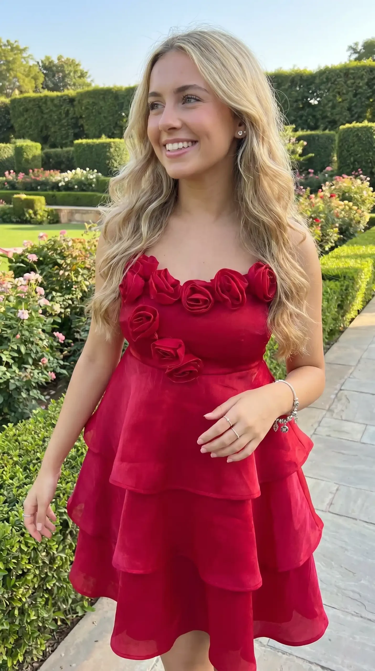 Woman wearing red 3D rosette strapless organza tiered mini dress in rose garden in summer