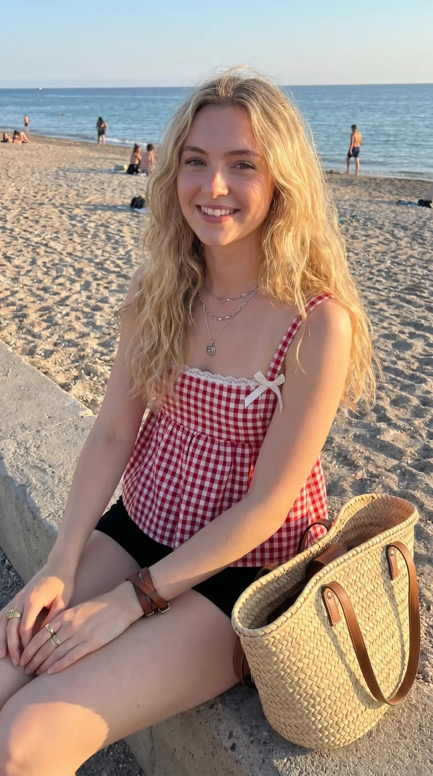 Woman wearing red gingham lace trim babydoll cami top with black shorts and woven tote bag at beach