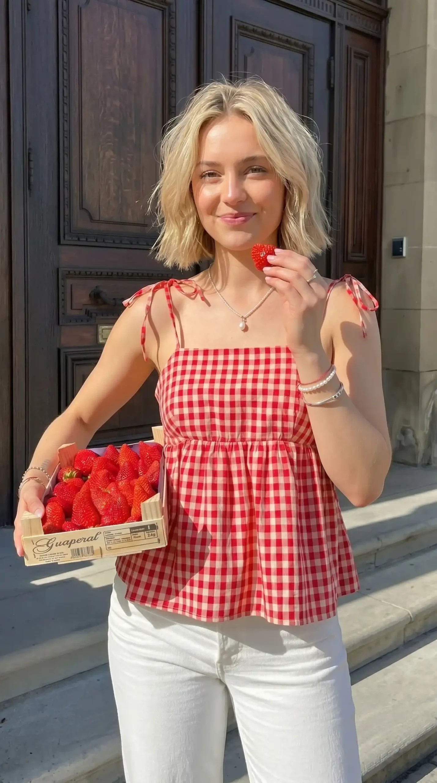 Woman wearing red and white gingham tie-strap babydoll top with white pants outdoors