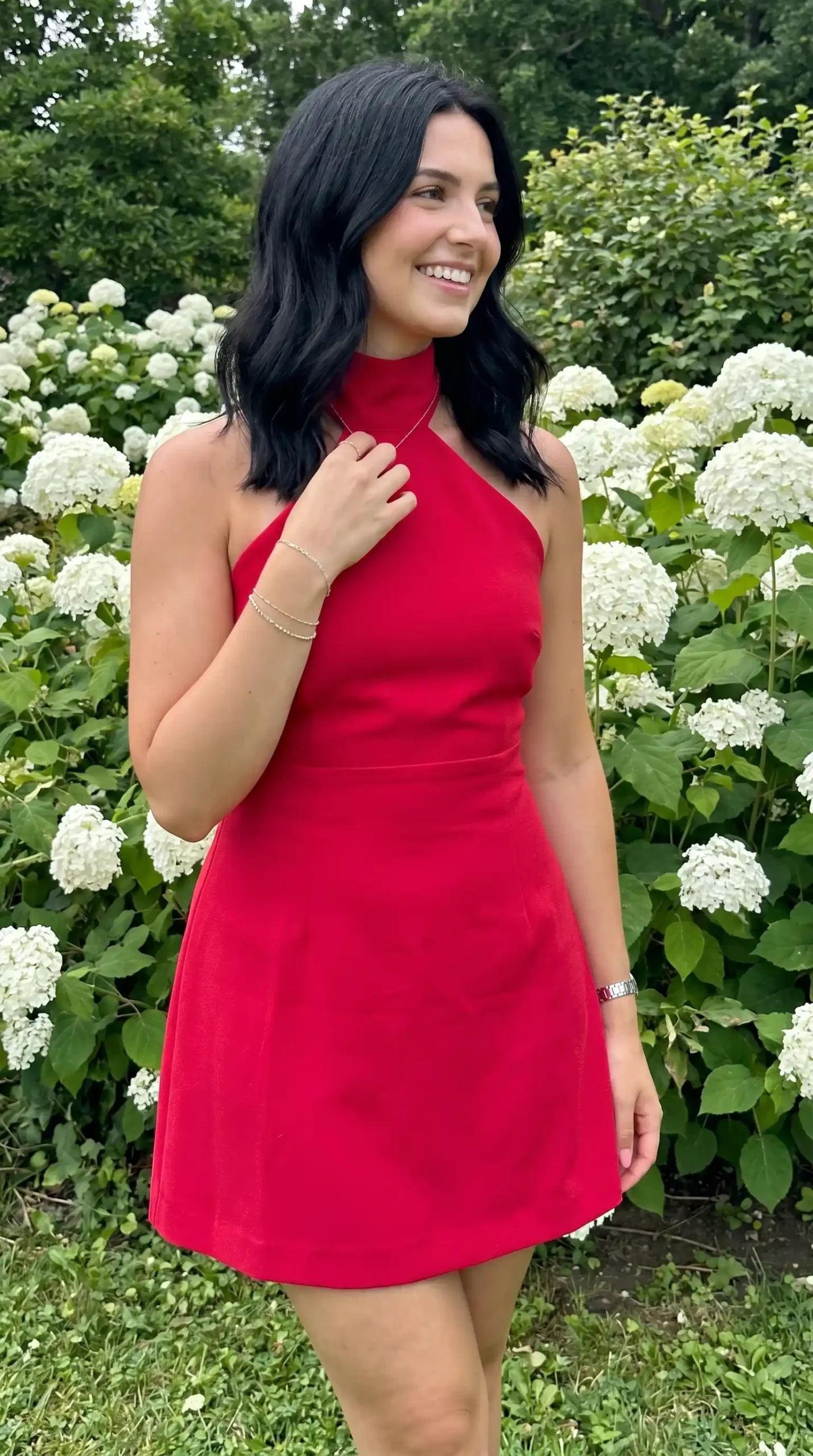 Woman wearing red halter neck A line mini dress in garden with white flowers in summer