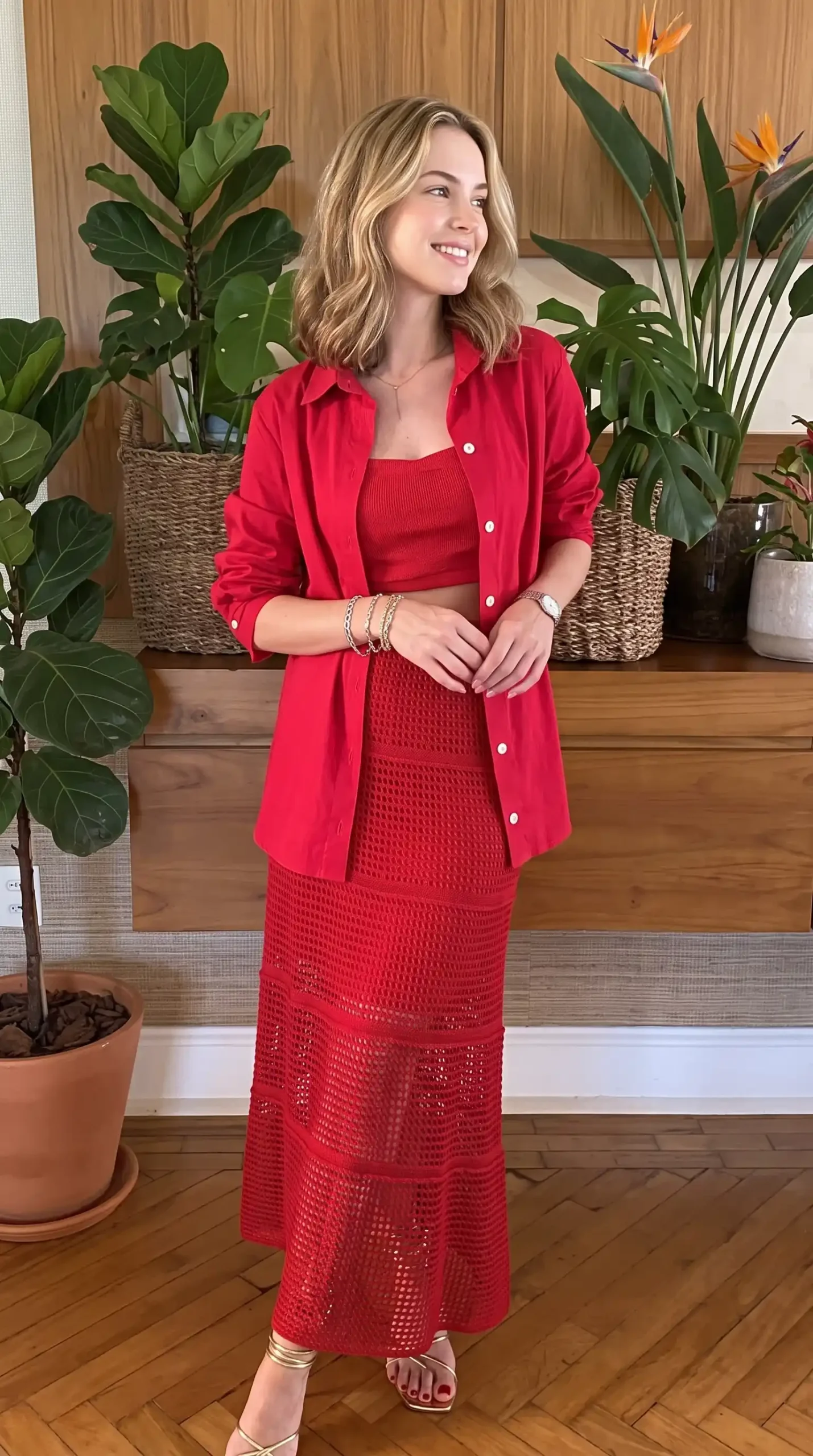Woman wearing red monochrome linen shirt with ribbed crop top and crochet maxi skirt indoors with plants