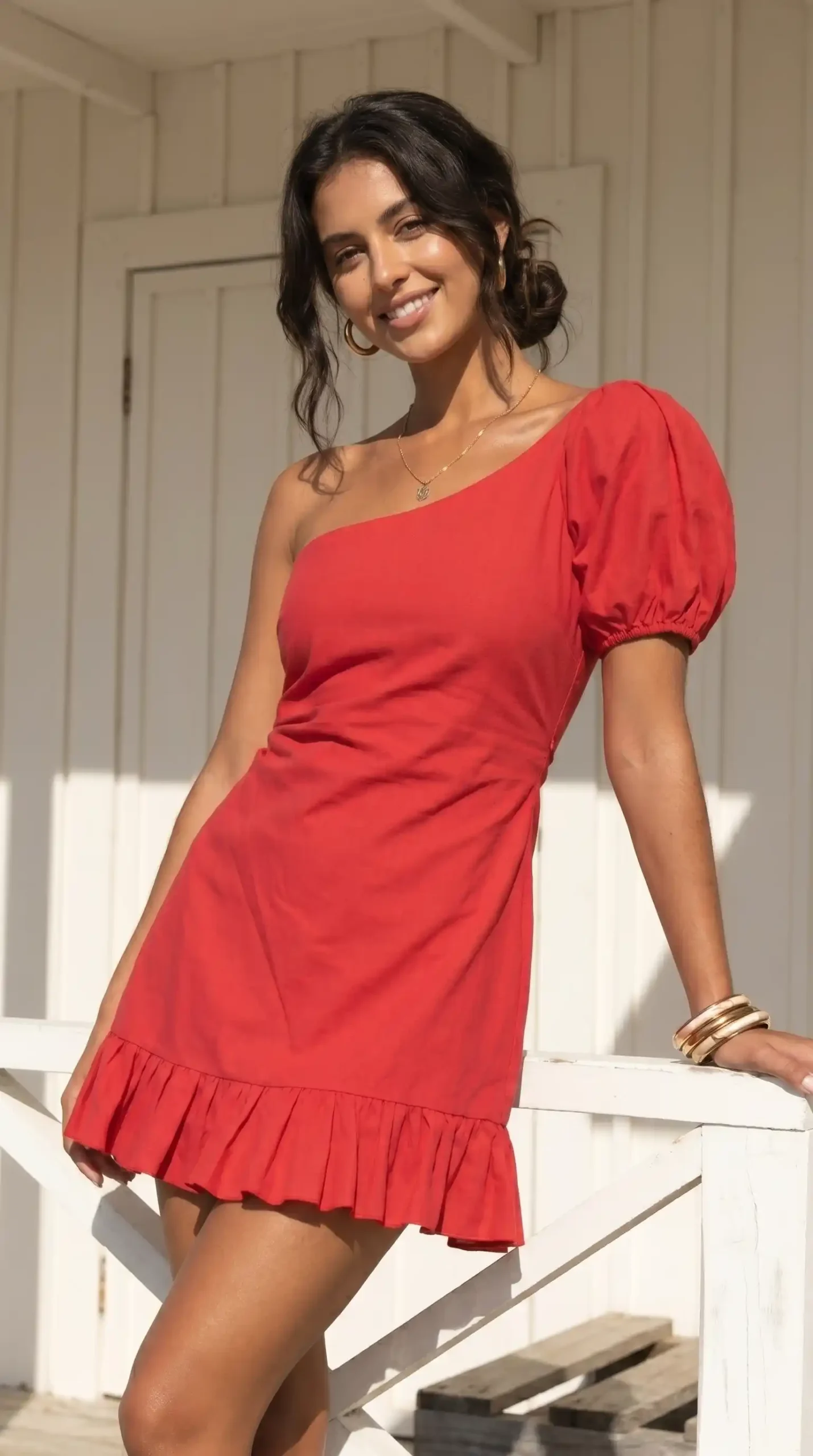 Woman wearing red one-shoulder puff sleeve mini dress with ruffle hem and gold bangles