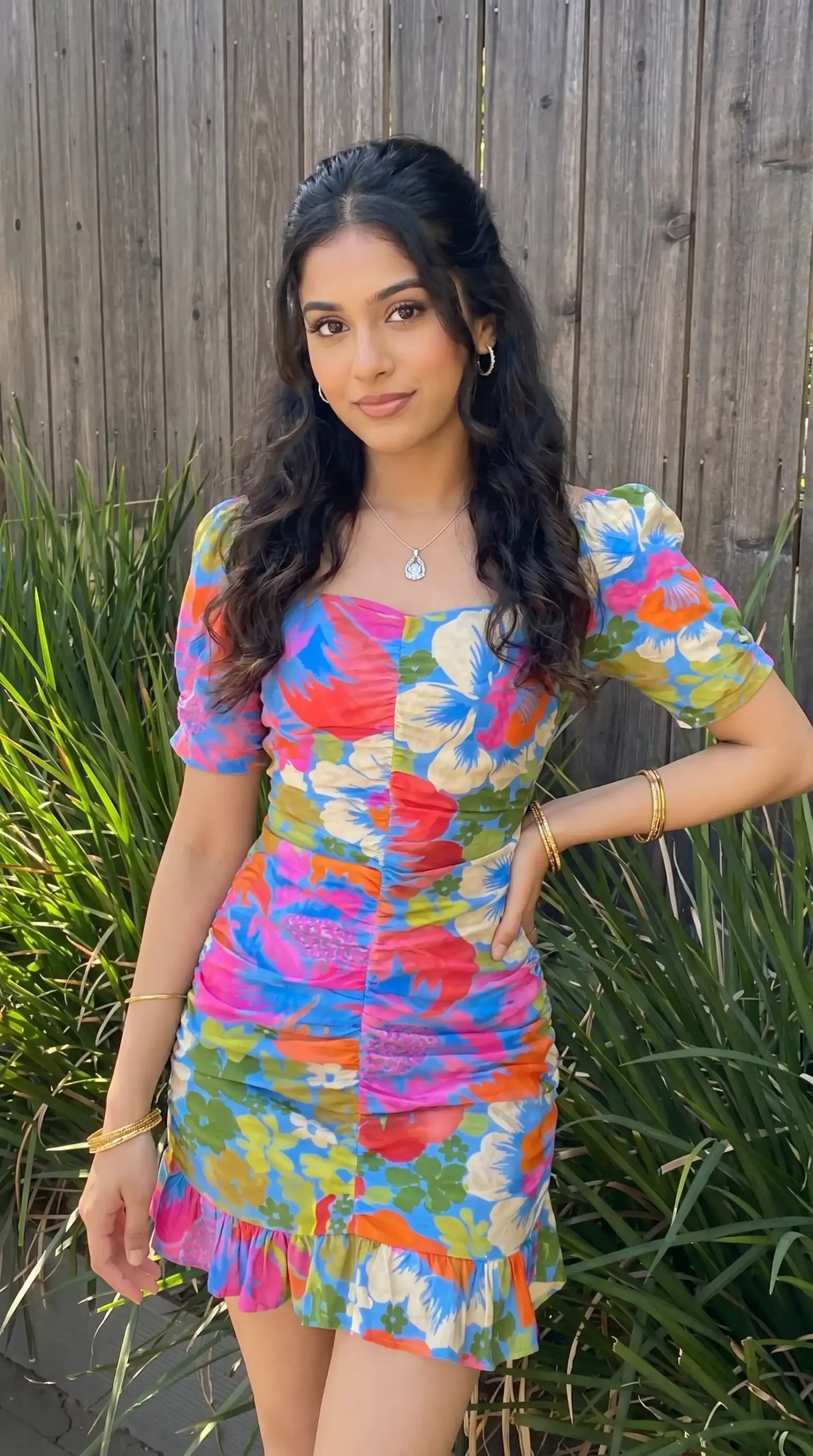 Woman wearing colorful floral print ruched mini dress in front of wooden fence